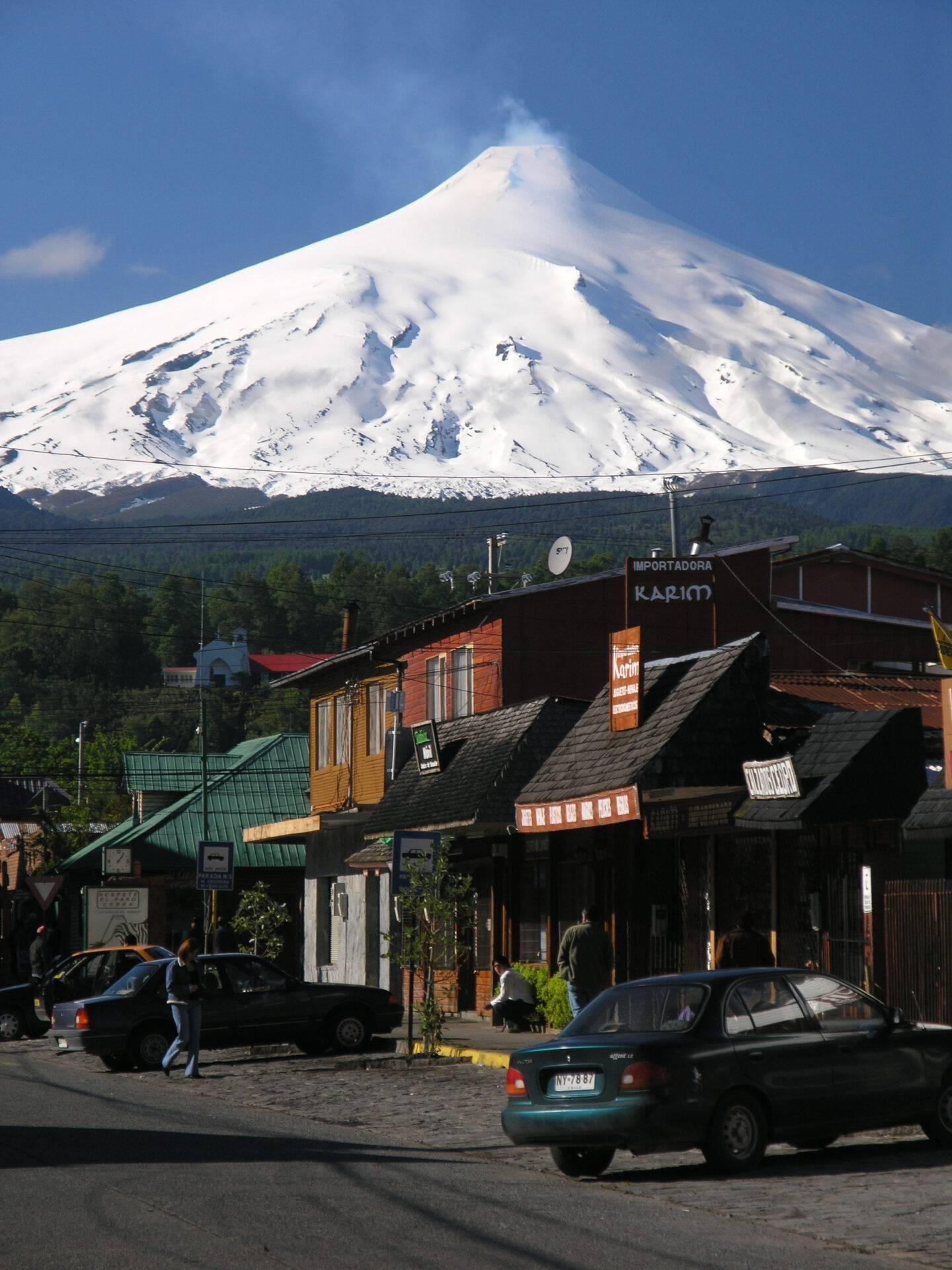 Une rue commerçante avec petits commerces en bois face à un volcan enneigé majestueux sous ciel bleu