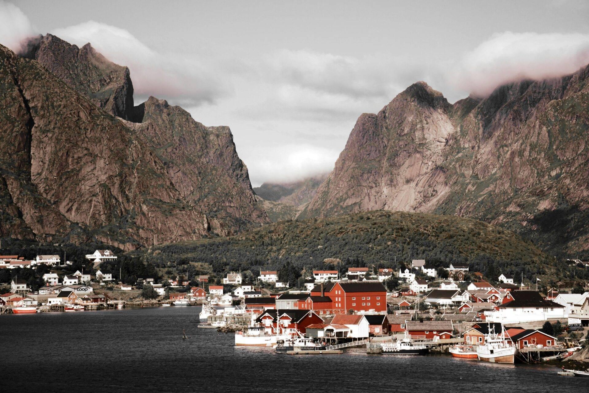 Un petit village côtier scandinave aux maisons rouges traditionnelles, encerclé par des montagnes escarpées et brouillard