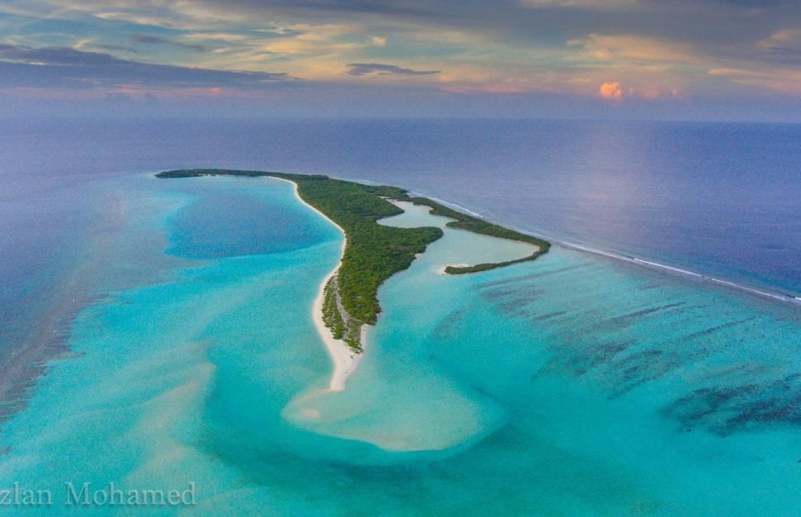 Vue aérienne d’une île tropicale avec lagon turquoise, plages de sable blanc et forêt verte dense