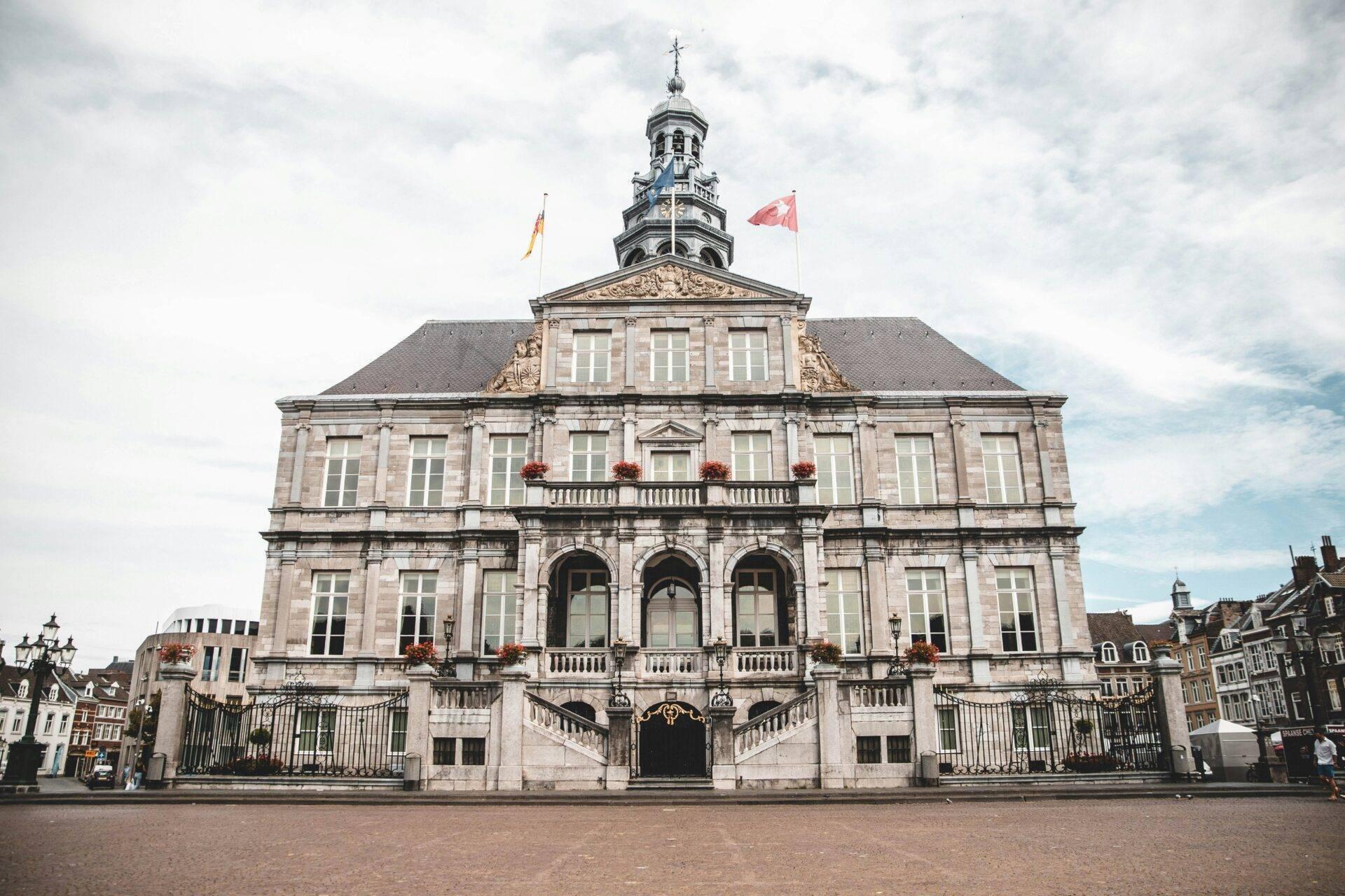 Un bâtiment administratif historique en pierre avec dôcher, drapeaux et balustrades, sur une place pavée