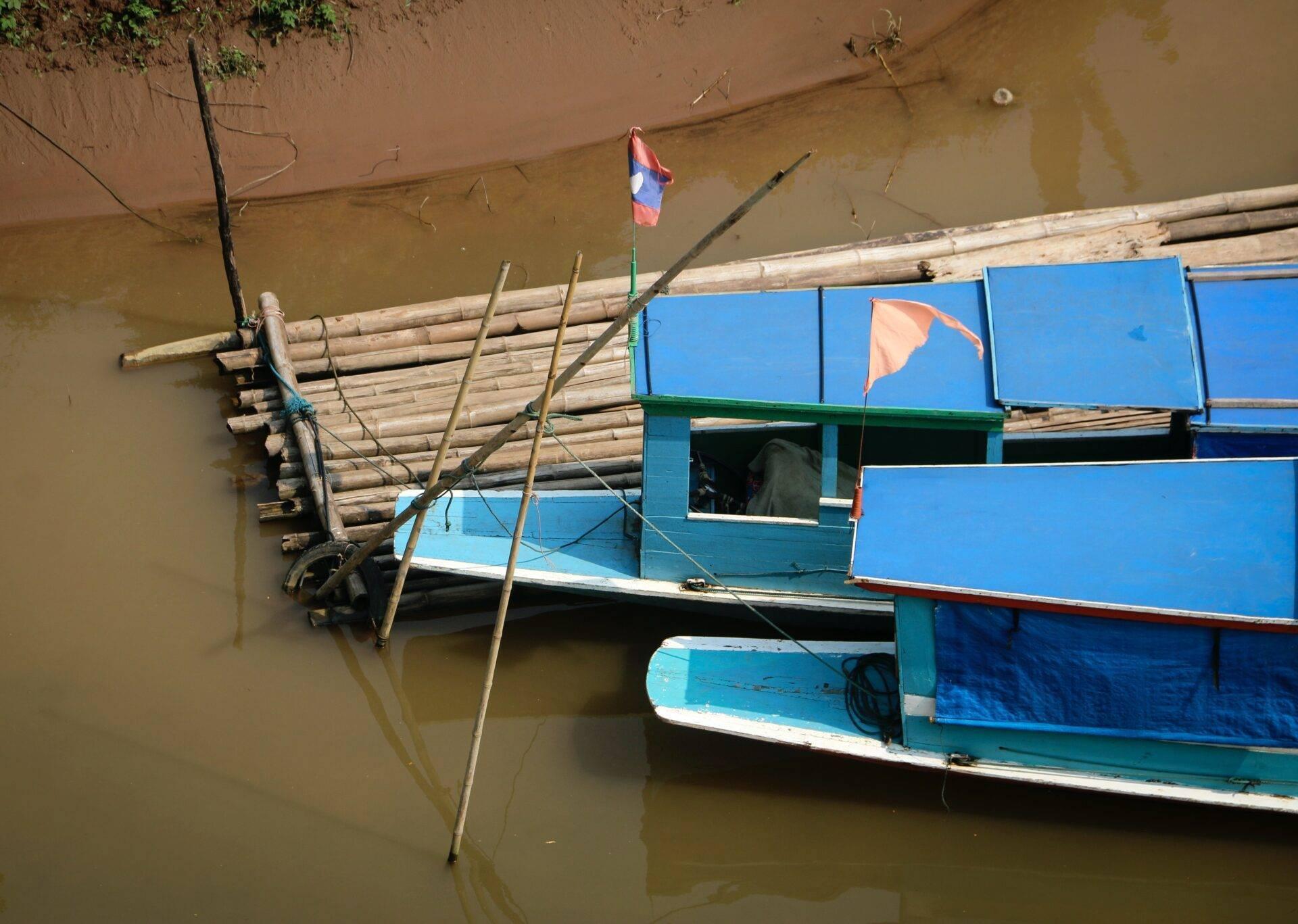 Bateaux de pêche traditionnels bleus amarrés dans une rivière boueuse avec drapeaux colorés