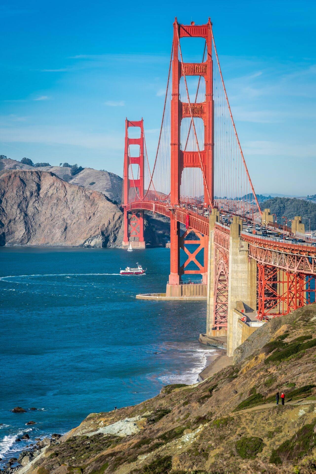 Un pont suspendu rouge iconic enjambant un détroit bleu avec collines rocheuses et un bateau au loin