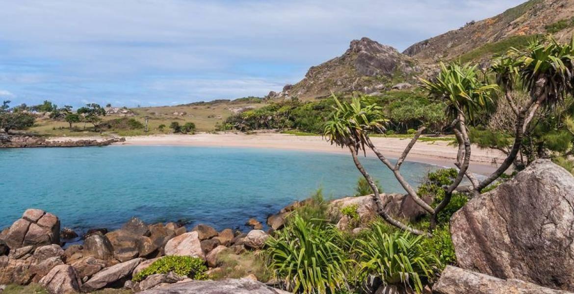 Une baie tropicale aux eaux turquoise bordée d’une plage de sable blanc, de rochers granitiques et de végétation verdoyante
