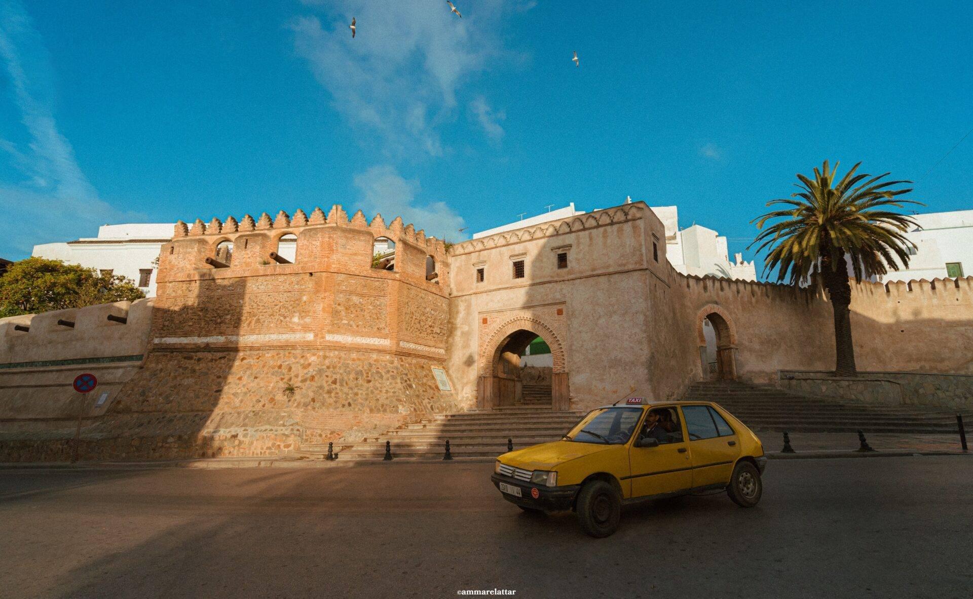 Un taxi jaune devant les remparts en pierre d’une médina marocaine sous un ciel bleu dégagé