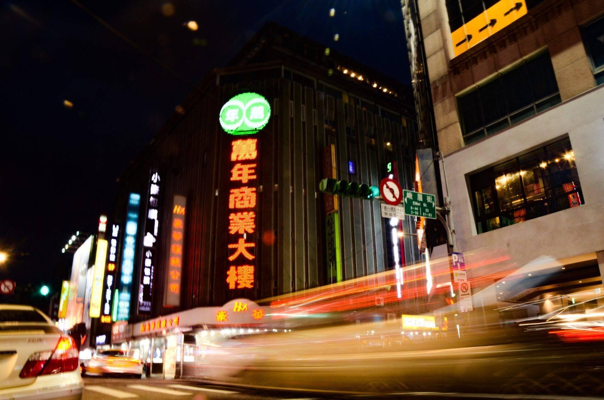 Une rue commerçante animée la nuit avec enseignes lumineuses en caractères chinois et circulation dense de véhicules