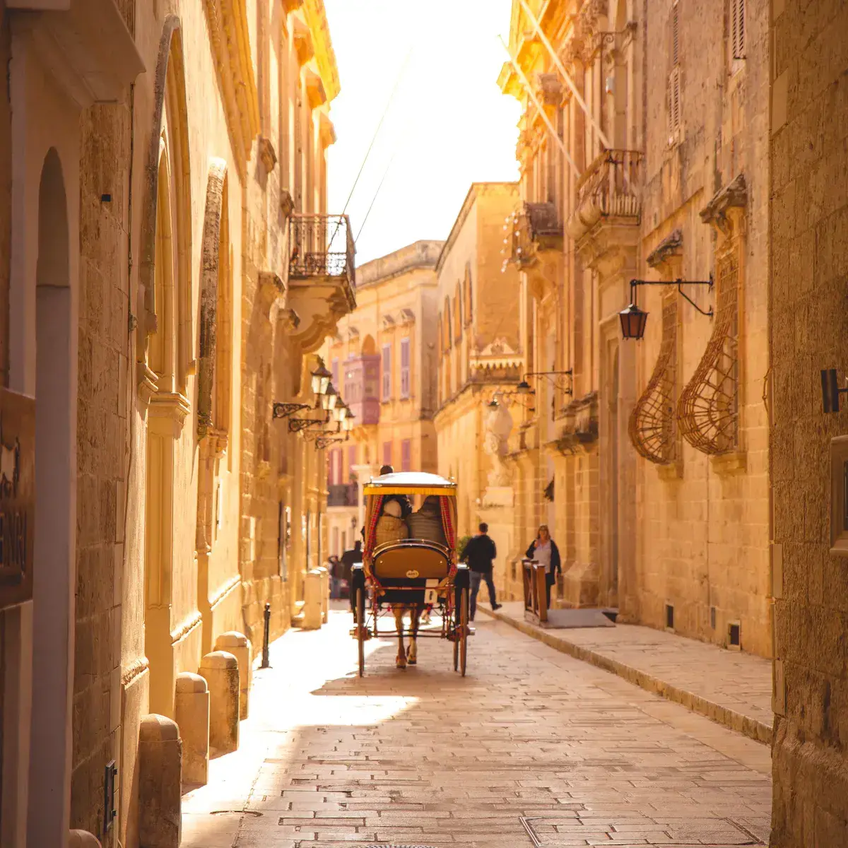 Une rue pavée étroite en pierre ocre avec un carrosse touristique, baignée de lumière chaude et encadrée par des façades historiques