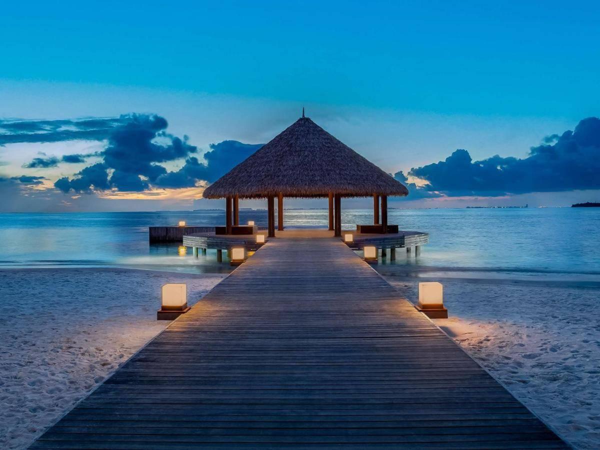 Un ponton en bois illuminé menant à un pavillon au toit de chaume sur une plage tropicale au crépuscule