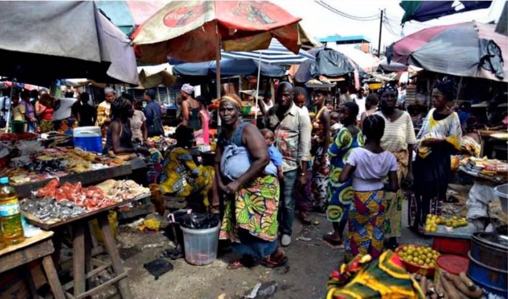 Un marché coloré en Afrique de l’Ouest avec vendeurs, étals de fruits et légumes, parapluies et foule animée