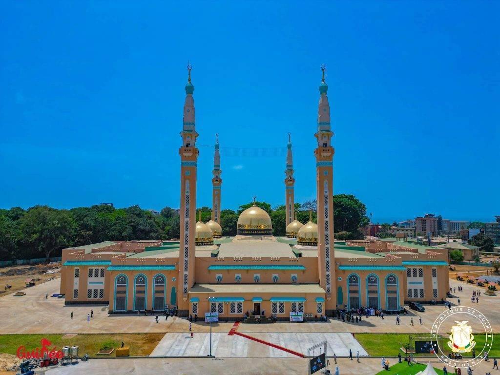 Une grande mosquée moderne avec dômes dorés et quatre minarets sous un ciel bleu dégagé