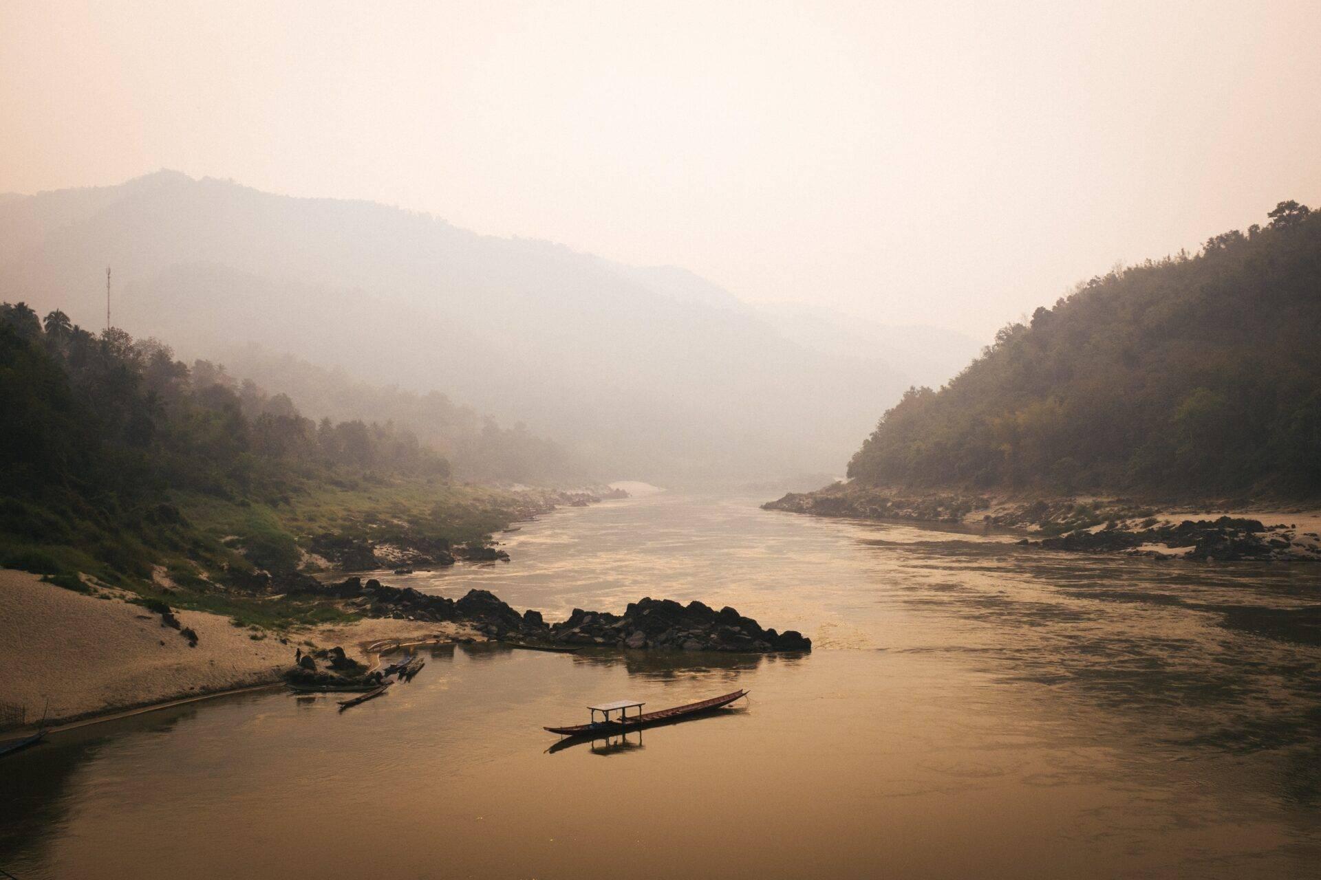 Deux barques traditionnelles sur un fleuve brumeux encadré de montagnes boisées et de brumes matinales