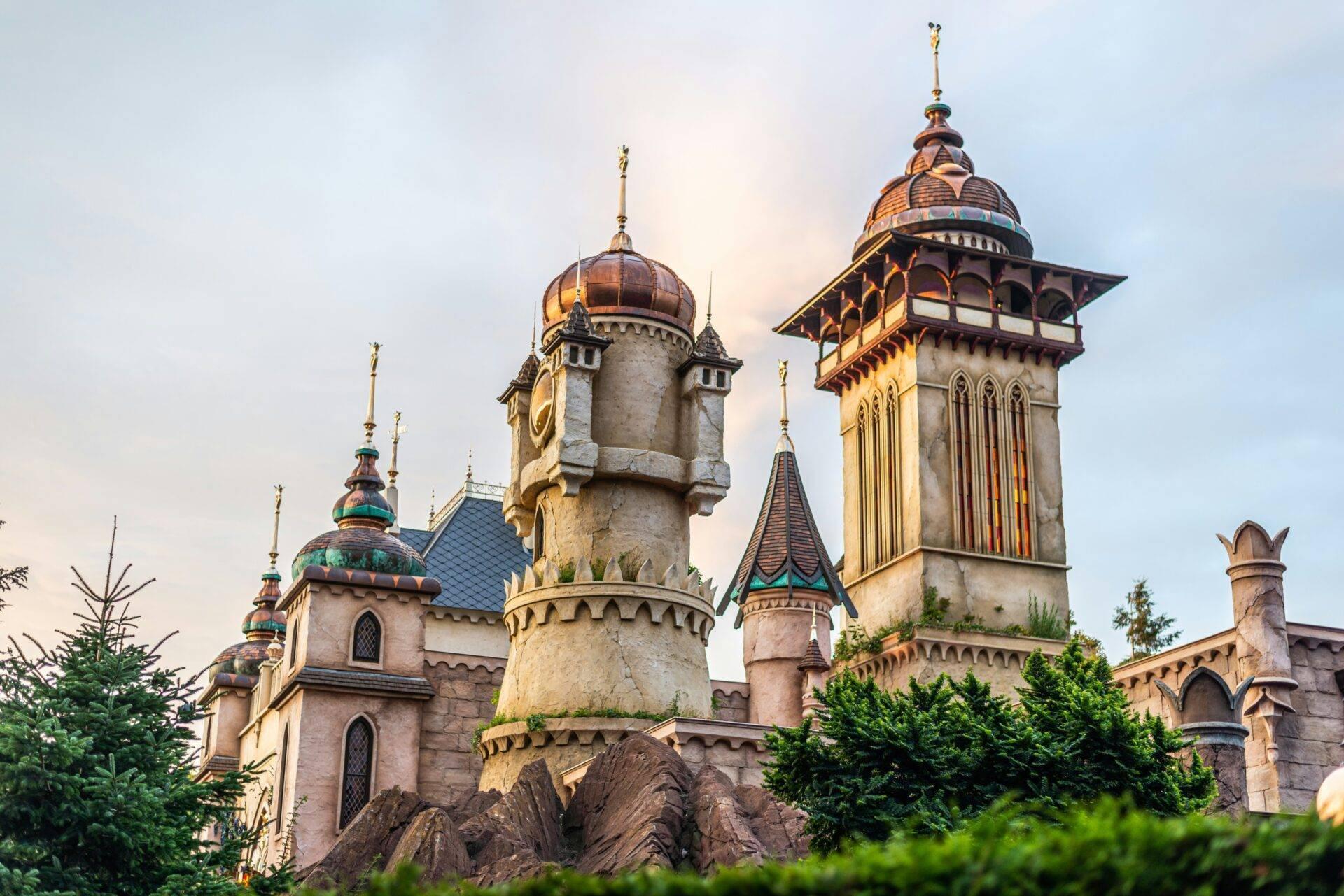 Un château de conte de fées avec tours dorées, dômes colorés et créneaux, entouré de verdure