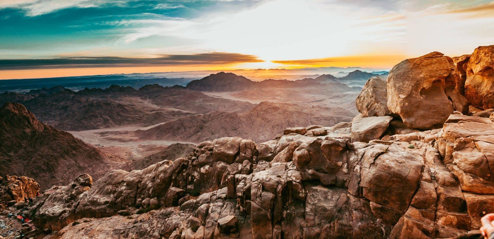 Vue panoramique d’un désert montagneux rocailleux au coucher de soleil, avec formations de granit en premier plan