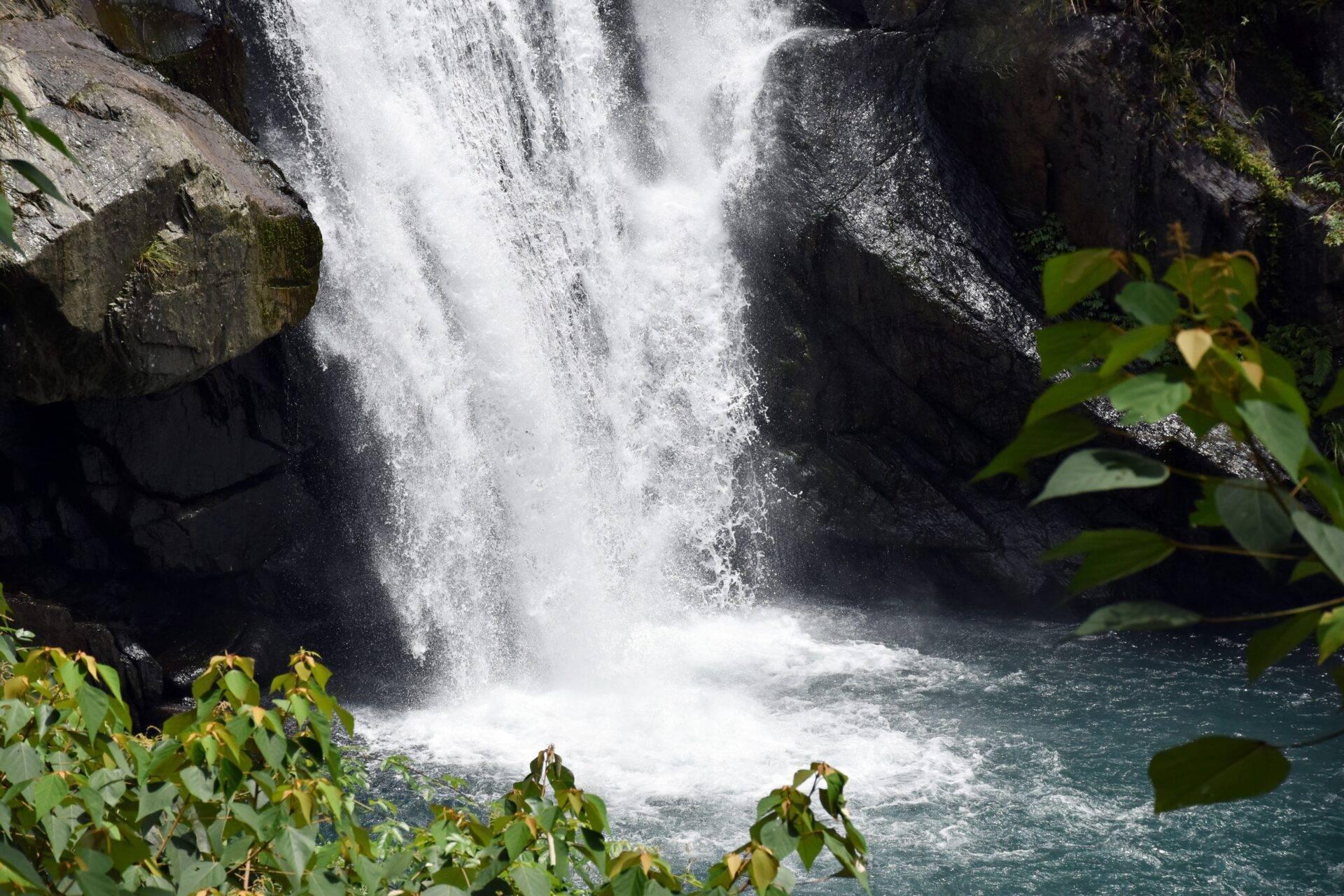 Une cascade puissante s’écoule dans un bassin turquoise entouré de roches moussues et de végétation luxuriante