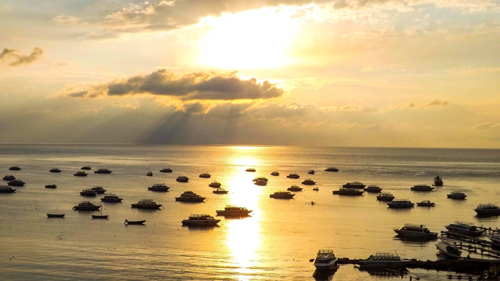 Coucher de soleil doré sur une baie avec de nombreuses barques de pêche ancrées dans des eaux calmes