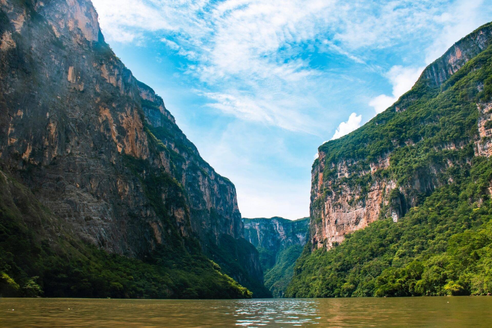 Un canyon spectaculaire aux parois rocheuses vertigineuses bordé de végétation luxuriante, traversé par une rivière