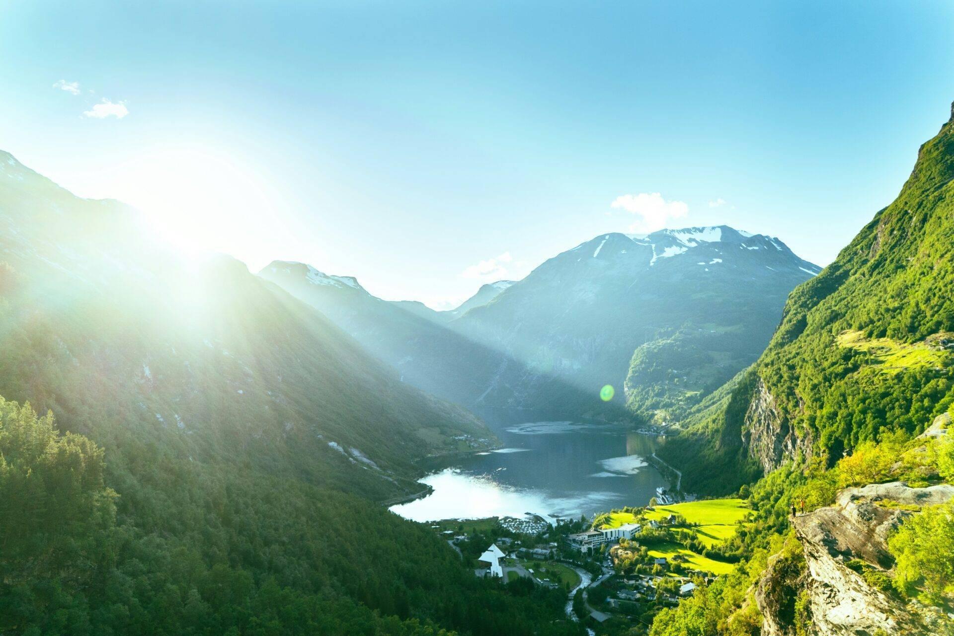 Vallée alpine avec lac bleu encaissé entre montagnes boisées et sommets enneigés sous soleil