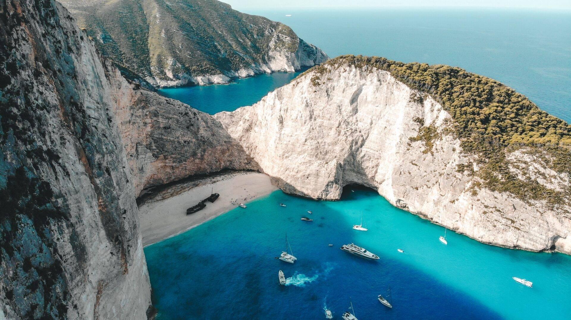 Vue aérienne d’une baie turquoise encadrée de falaises blanches avec plage et bateaux ancrés