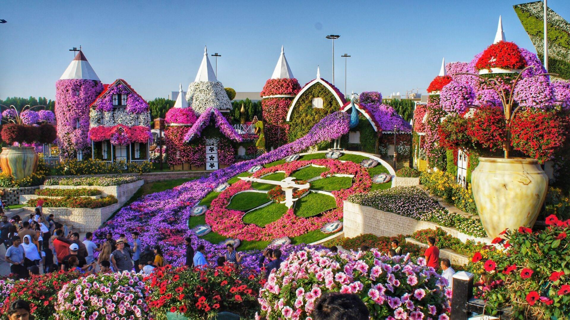 Un parc floral spectaculaire avec des bâtiments décorés de millions de fleurs colorées et des visiteurs admirant les installations