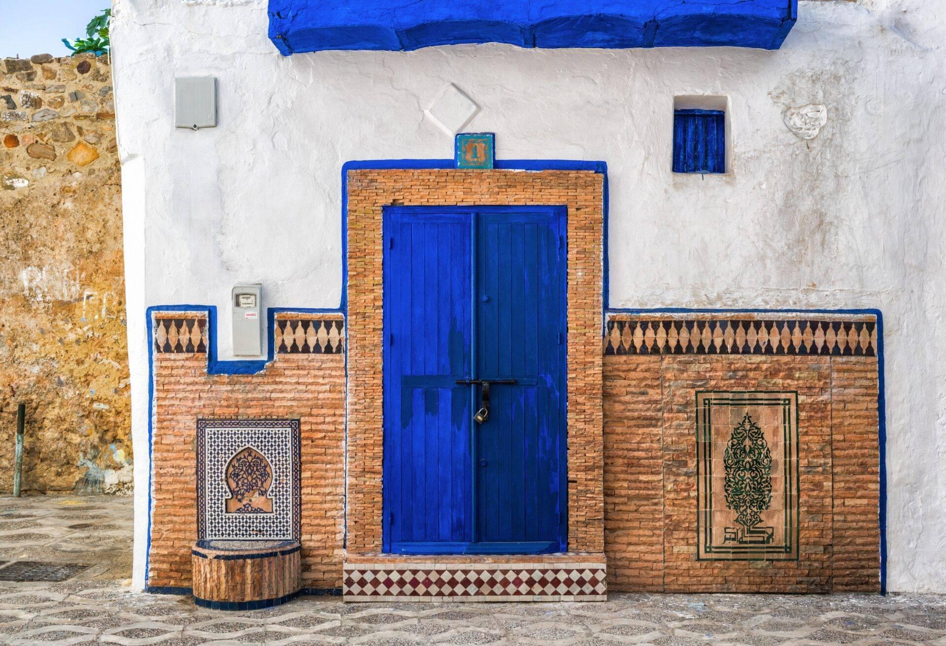 Façade traditionnelle marocaine avec porte bleue, détails en zellige et brique rouge, blanc et bleu caractéristiques