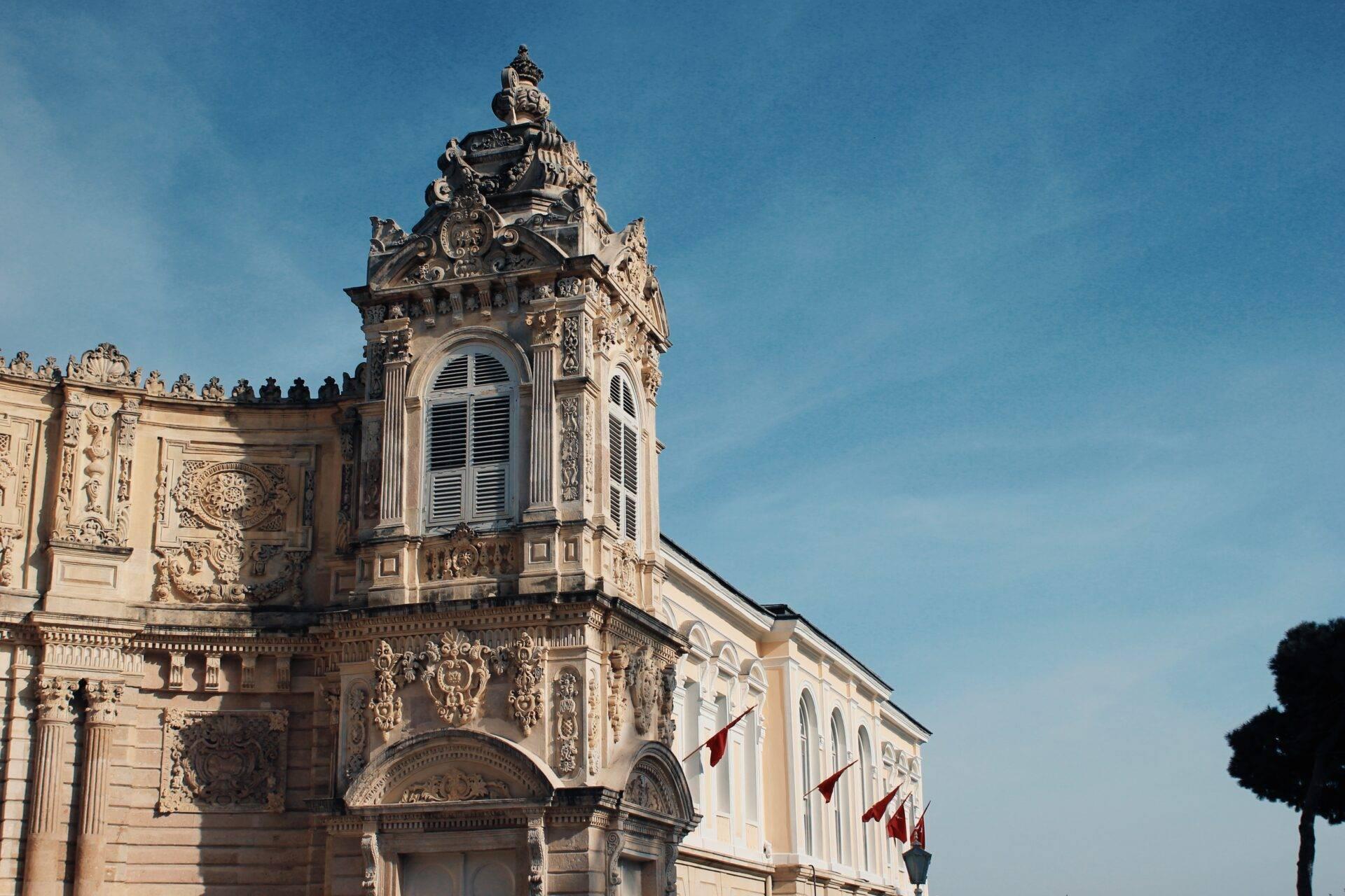 Façade ornementée d’un bâtiment historique avec tour élaborée et drapeaux rouges sous ciel bleu