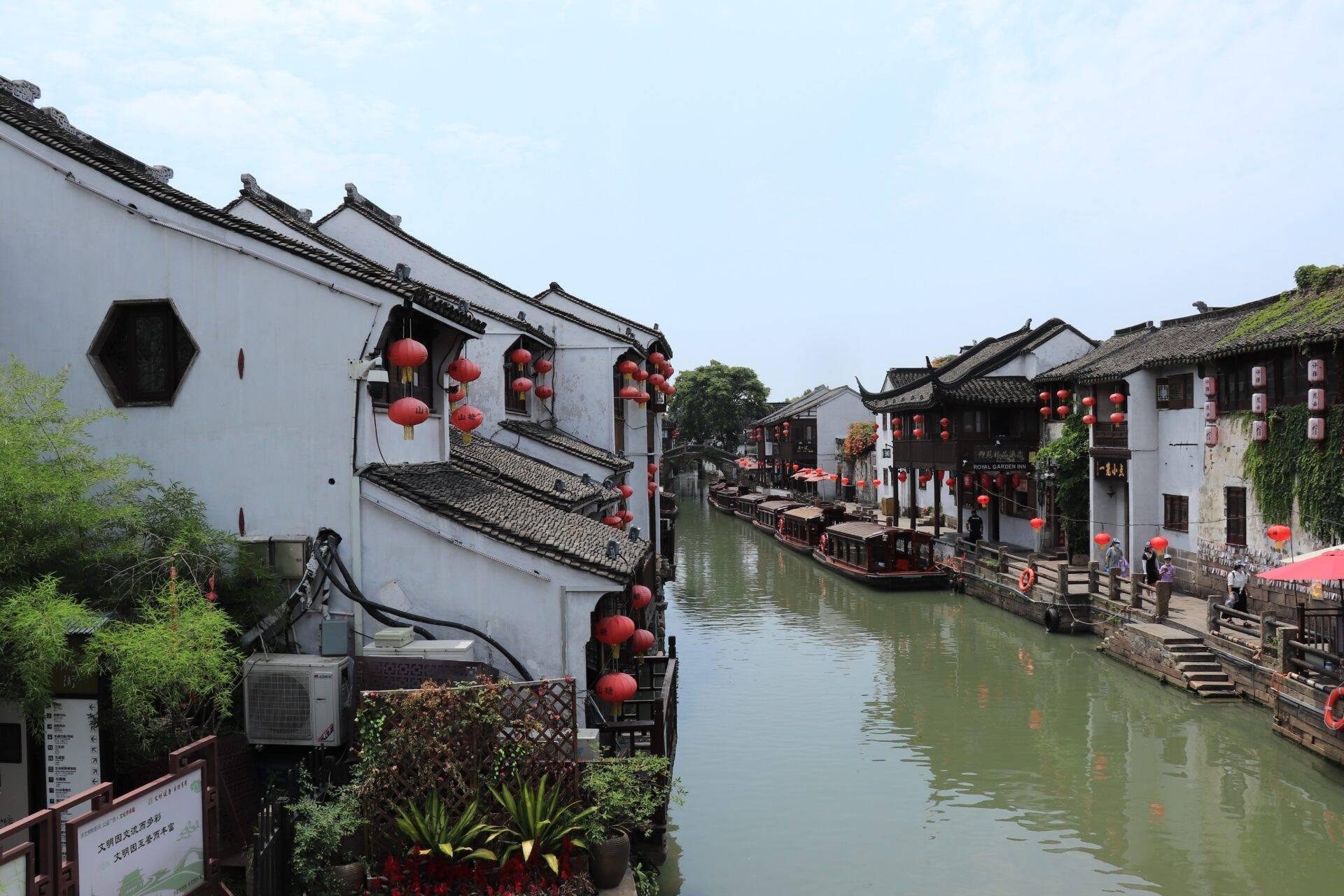Village ancien chinois avec canal, architecture traditionnelle blanche et noire, lanternes rouges, et bateaux de tourisme