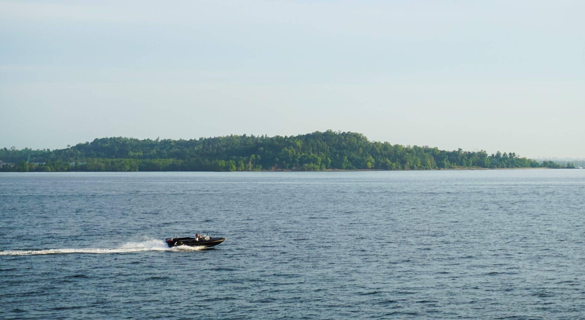 Un bateau à moteur navigue sur un lac aux eaux calmes bordé d’une forêt dense et verdoyante