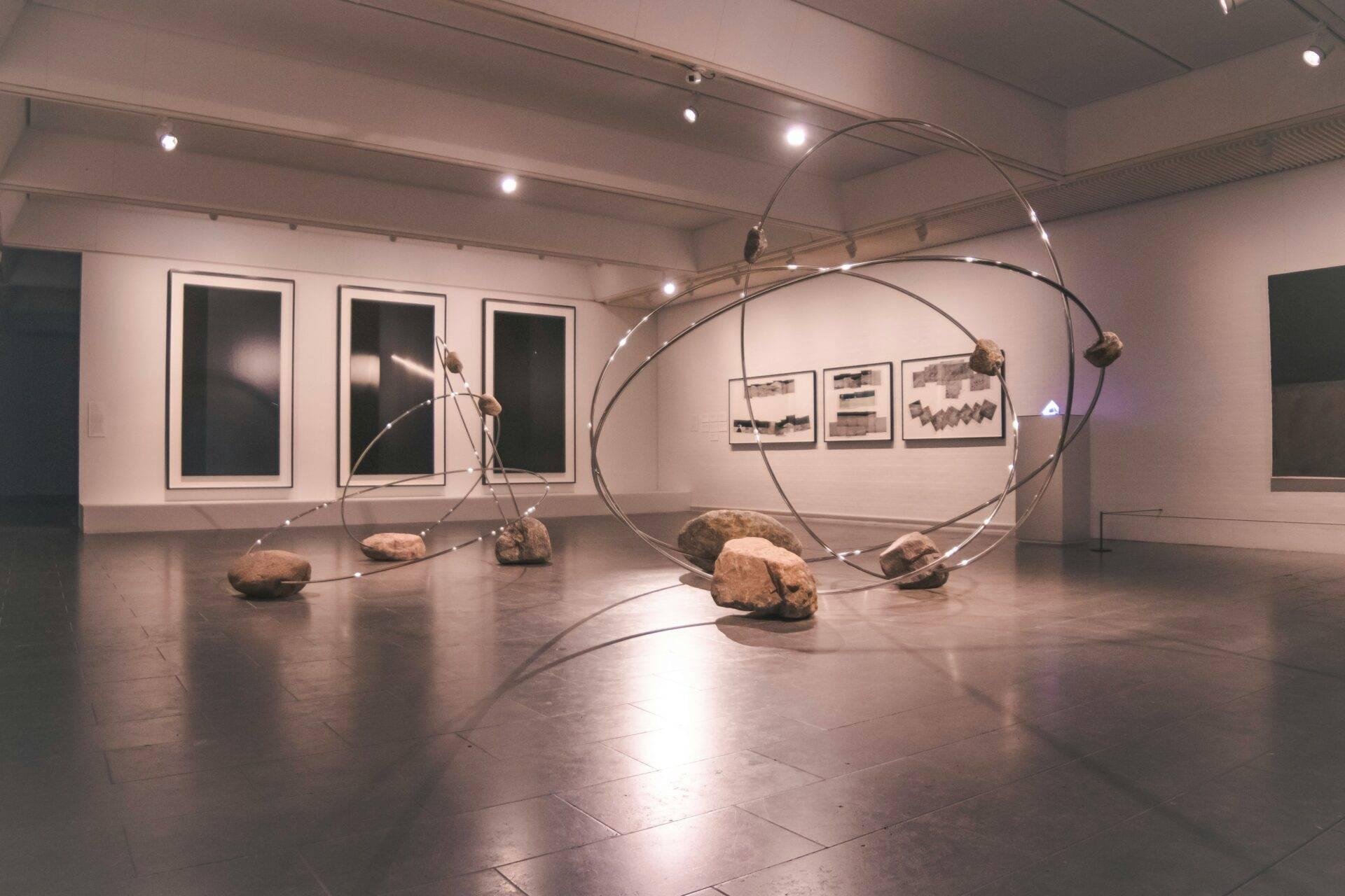 Installation artistique contemporaine avec structures métalliques courbes et rochers dans une galerie d’art minimaliste