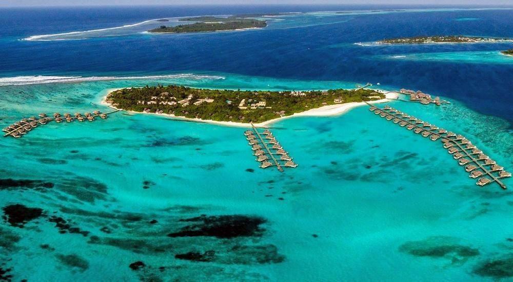 Vue aérienne d’une île tropicale entourée de bungalows sur pilotis dans un lagon turquoise aux eaux cristallines