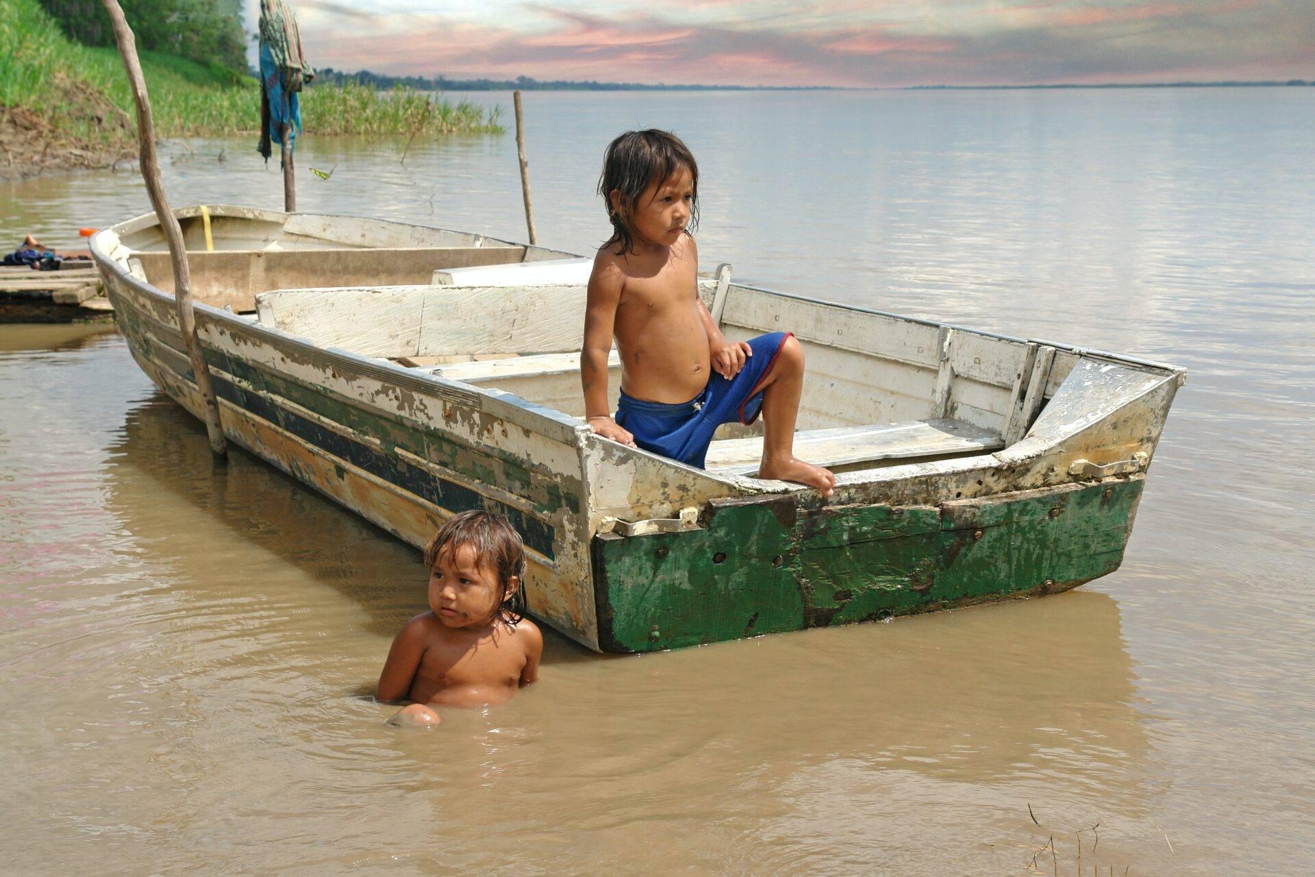 Deux enfants jouent dans l’eau près de vieux bateaux de pêche en bois à proximité d’une côte marécageuse