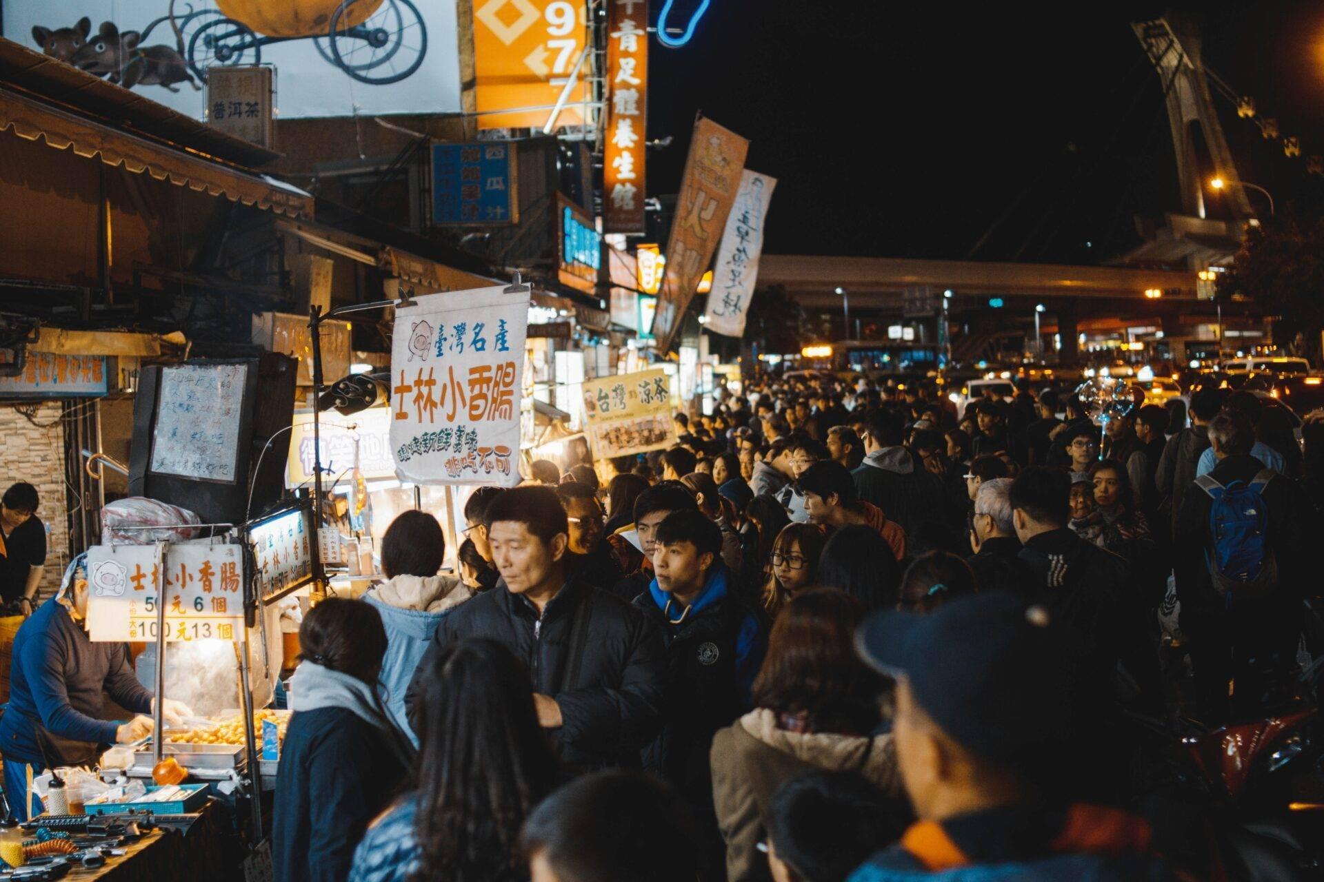 Une rue commerçante animée de nuit avec des vendeurs de street food et une foule dense sous des enseignes lumineuses en caractères chinois