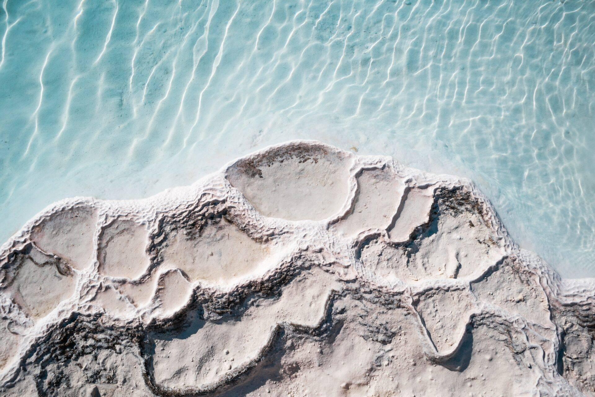 Vue aérienne d’une formation géologique blanche et érodée bordée par une eau turquoise cristalline