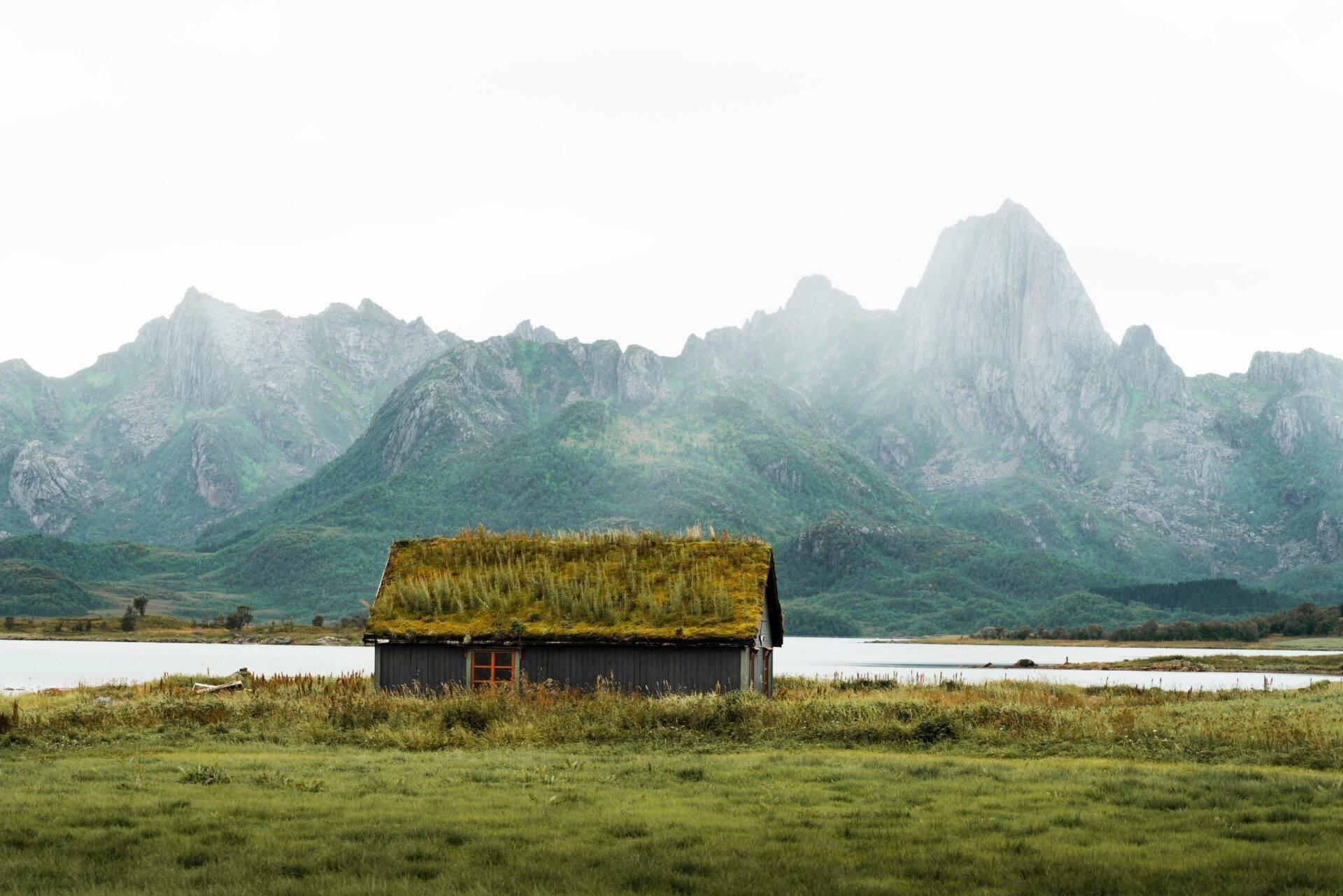 Une cabane au toit de mousse devant un lac et des montagnes rocheuses verdoyantes en Norvège