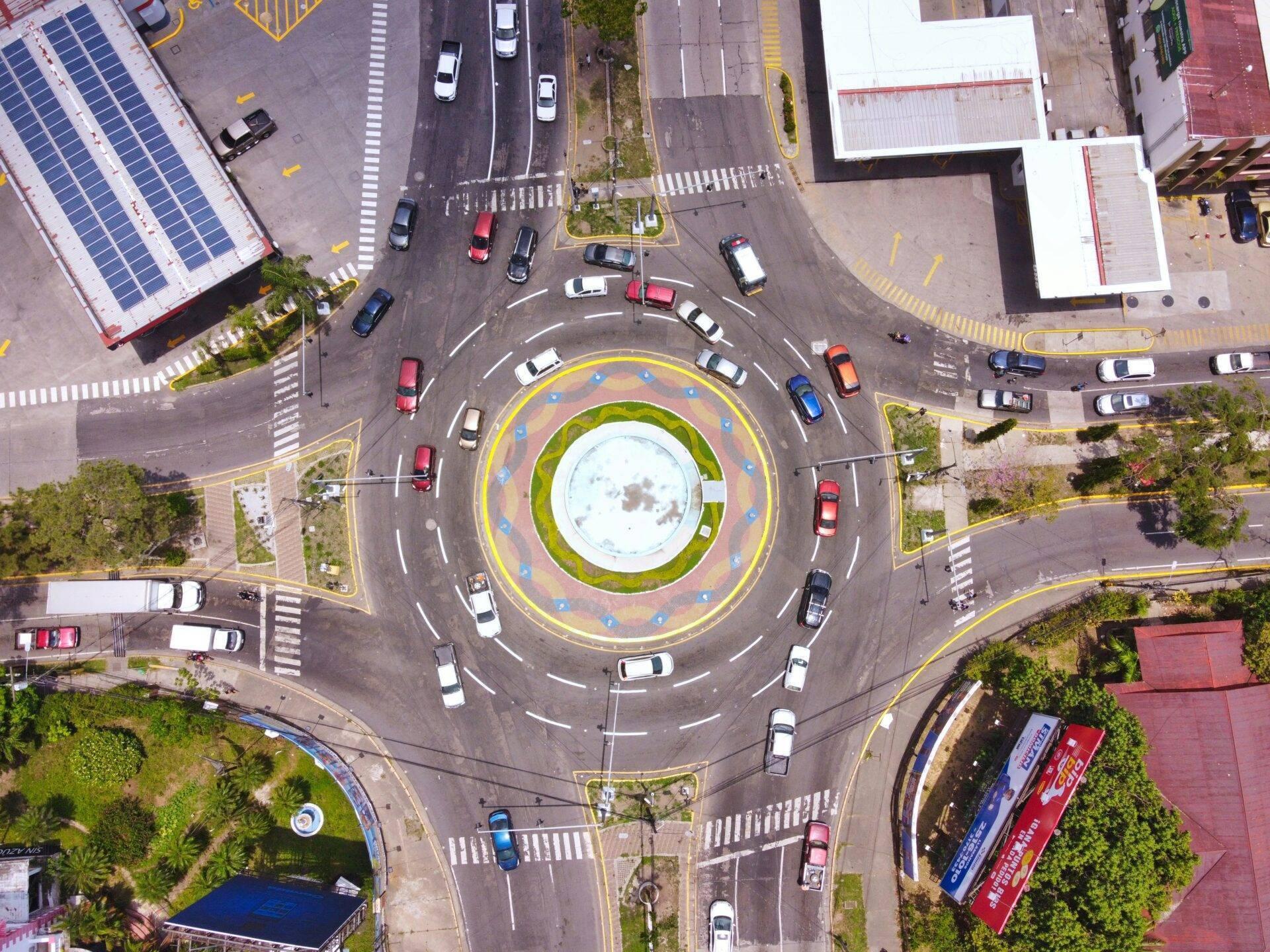 Vue aérienne d’un rond-point urbain avec fontaine centrale, voitures et bâtiments environnants avec toits solaires