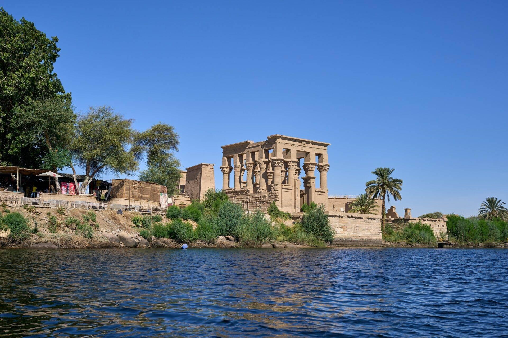 Ruines d’un temple antique au bord du Nil avec colonnes imposantes et palmiers sous ciel bleu dégagé