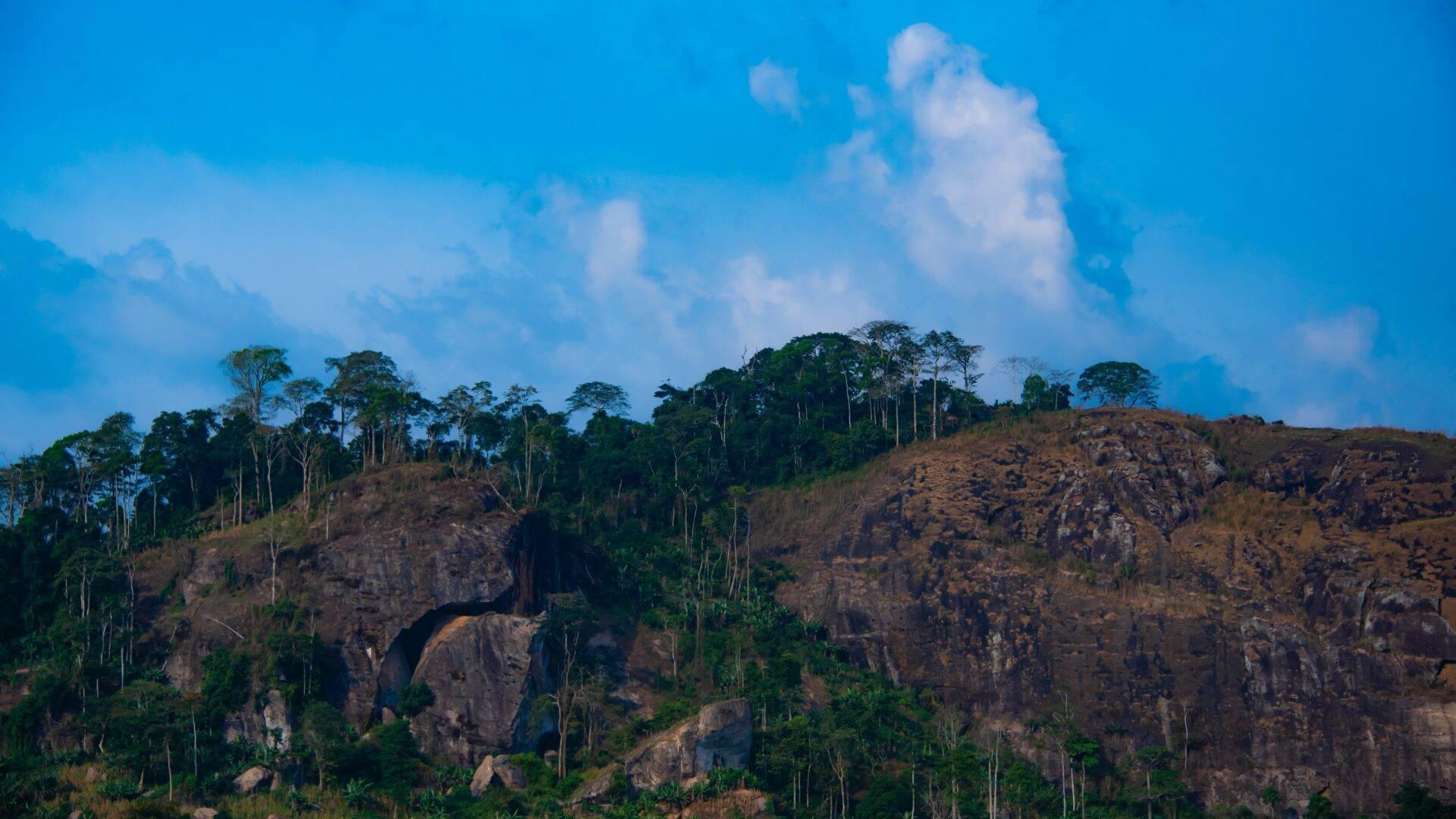 Paysage montagneux avec affleurements rocheux, végétation tropicale dense et ciel bleu nuageux