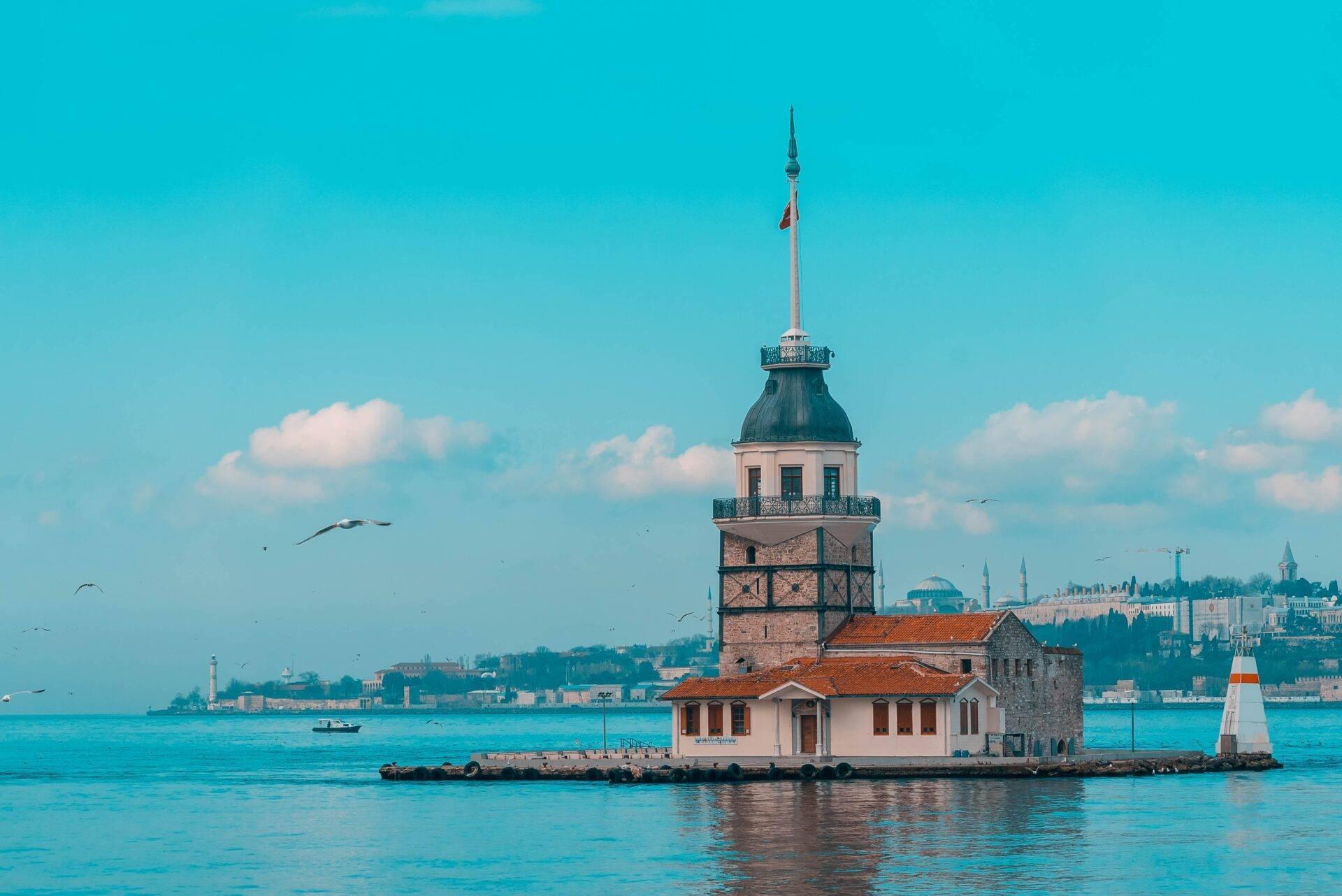 Une tour historique avec minaret au cœur d’un détroit turquoise, entourée de la mer et de la ville côtière en arrière-plan