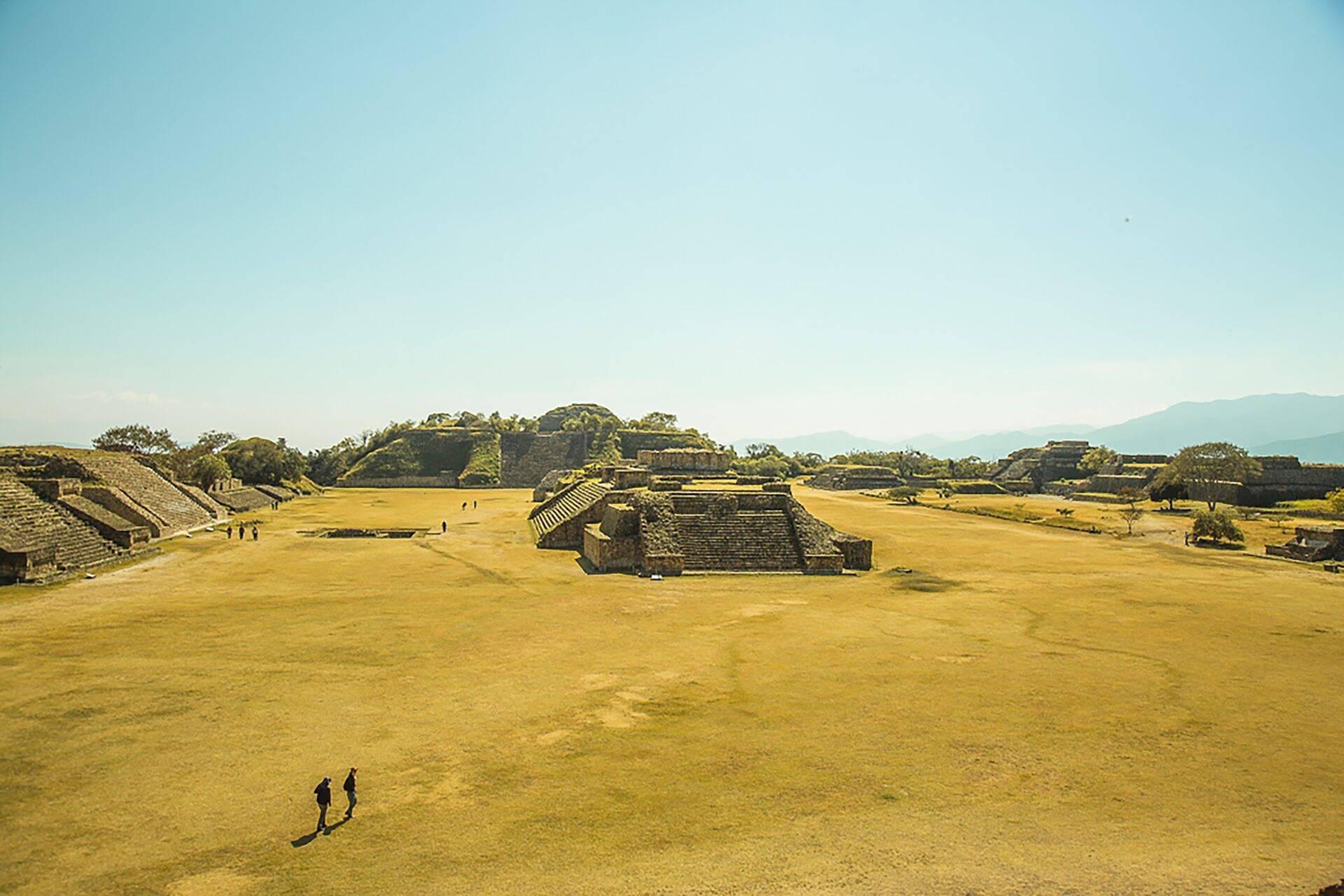 Une vaste esplanade archéologique avec pyramides préhispaniques entourées de montagnes verdoyantes en arrière-plan