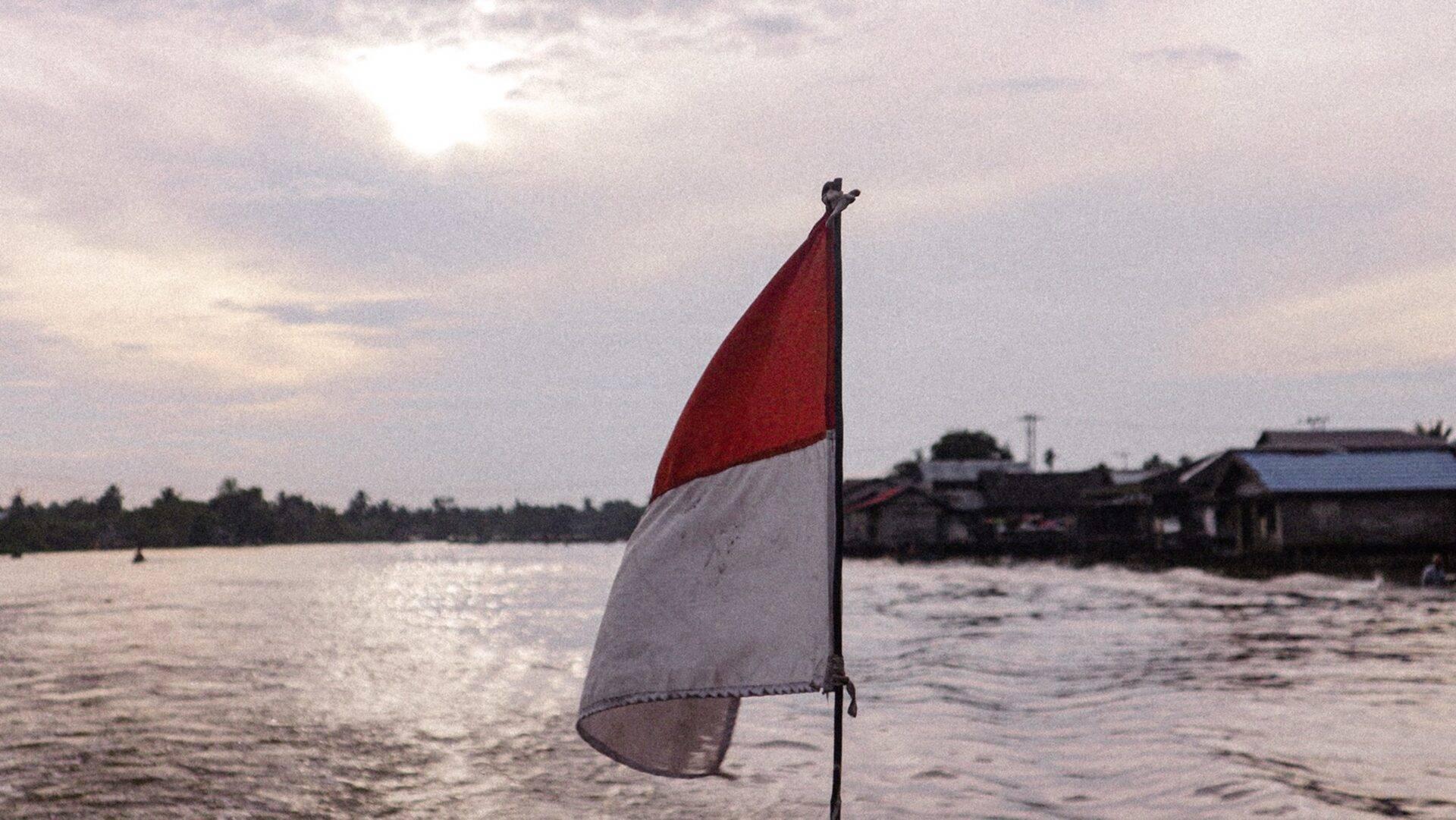 Drapeau rouge et blanc flottant au-dessus d’une rivière avec des maisons traditionnelles en arrière-plan