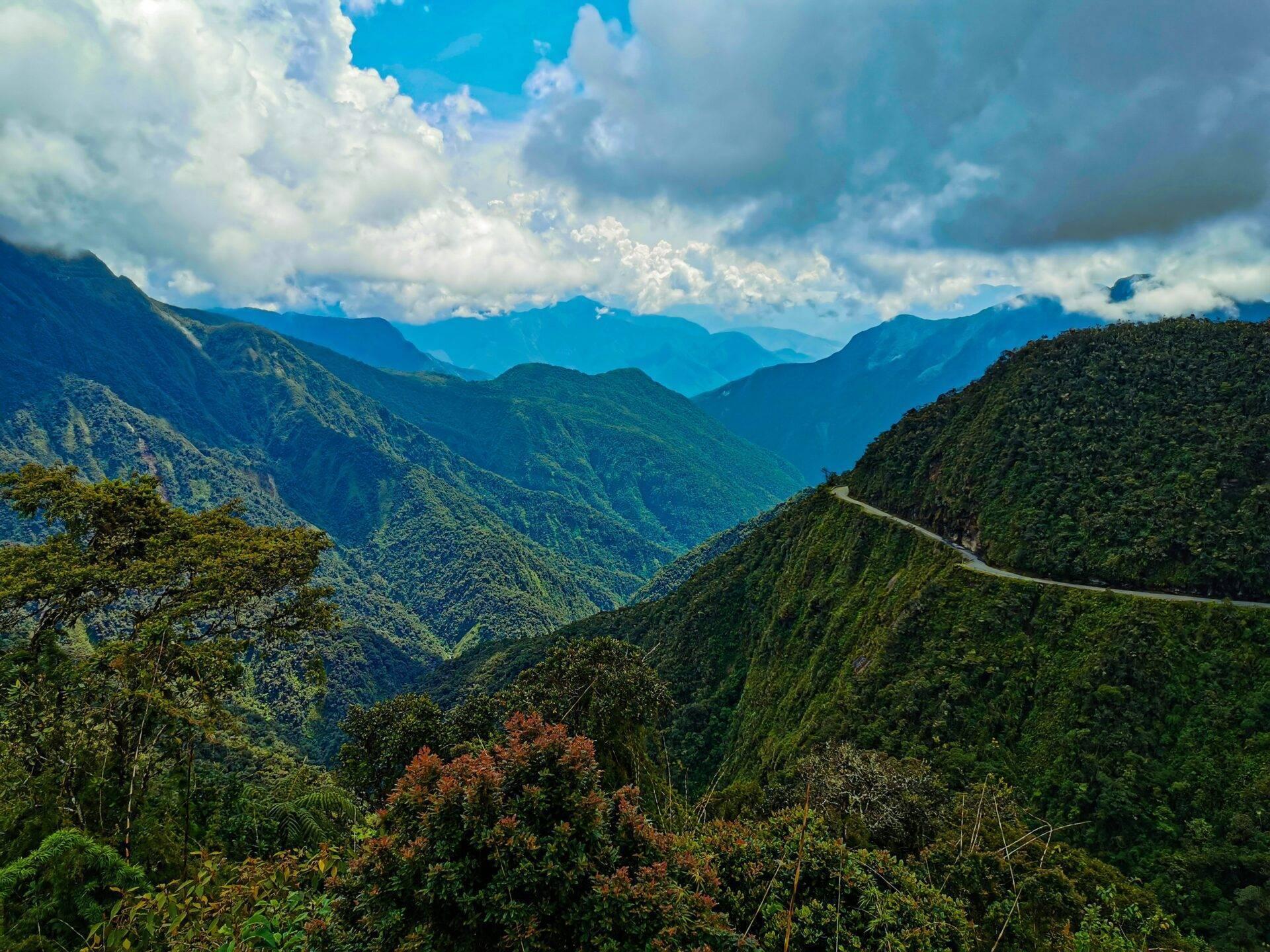Chaîne de montagnes densément boisées avec route sinueuse et ciel nuageux, paysage montagneux tropical