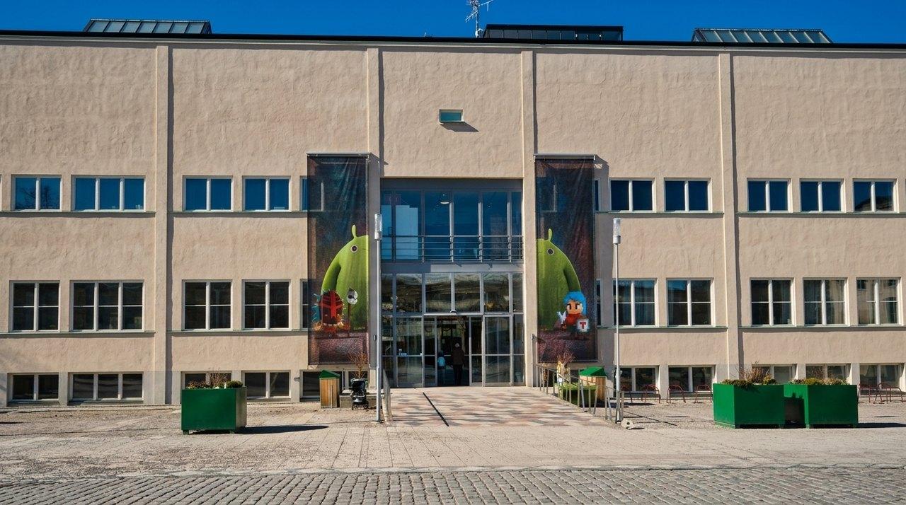 Façade moderne d’un bâtiment institutionnel avec entrée centrale vitrée et fresques colorées pour enfants sur les panneaux latéraux