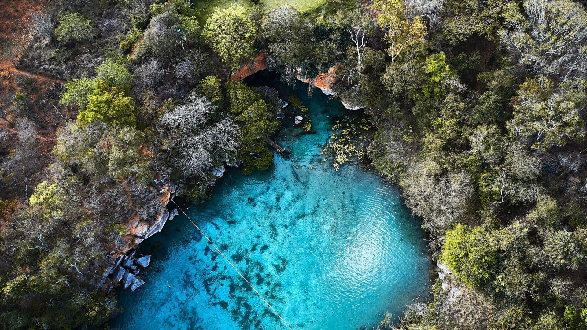 Vue aérienne d’un bassin d’eau turquoise entouré de forêt dense et de falaises rocheuses