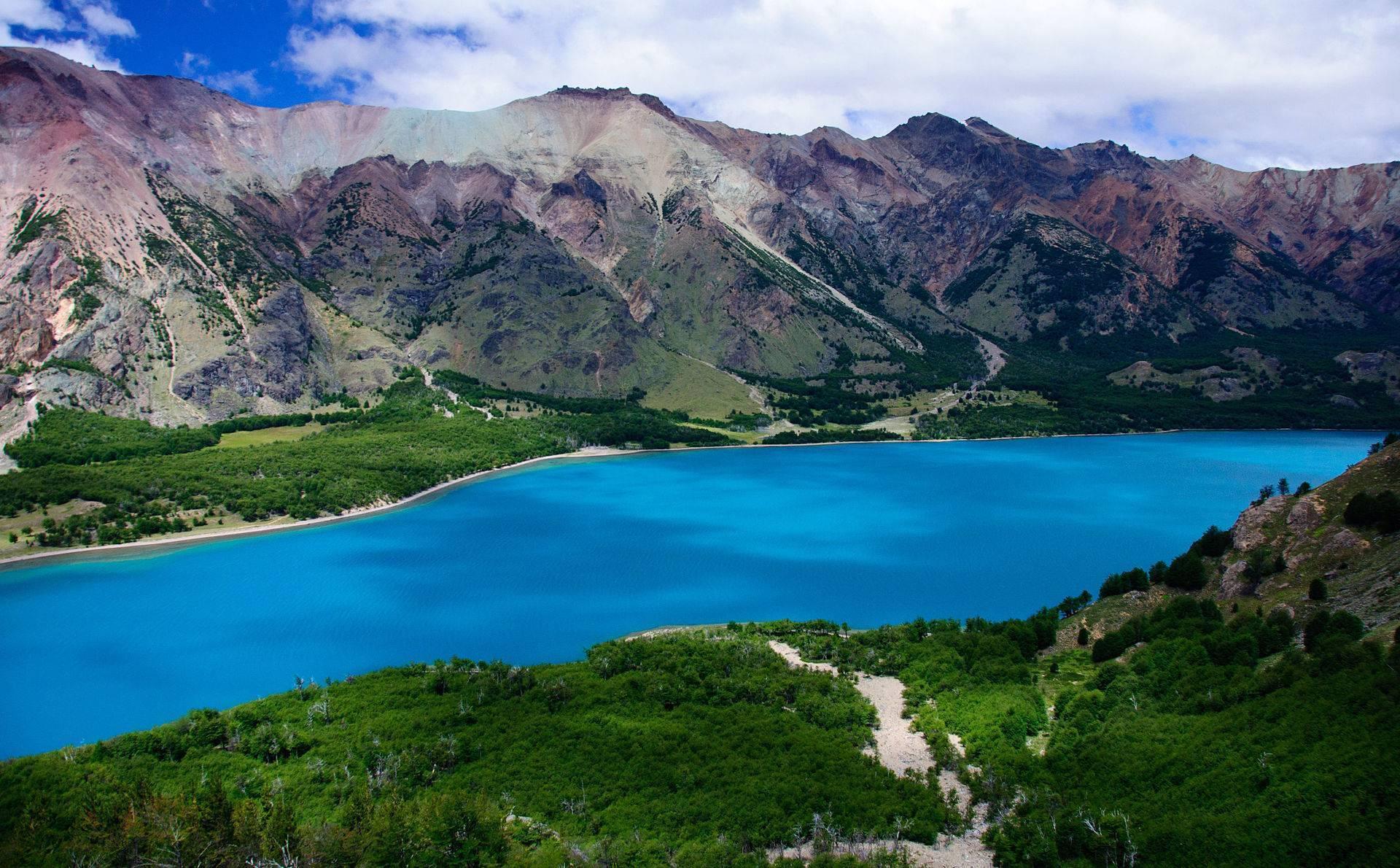 Lac de montagne aux eaux turquoise entouré de pics rocheux colorés et de végétation verdoyante