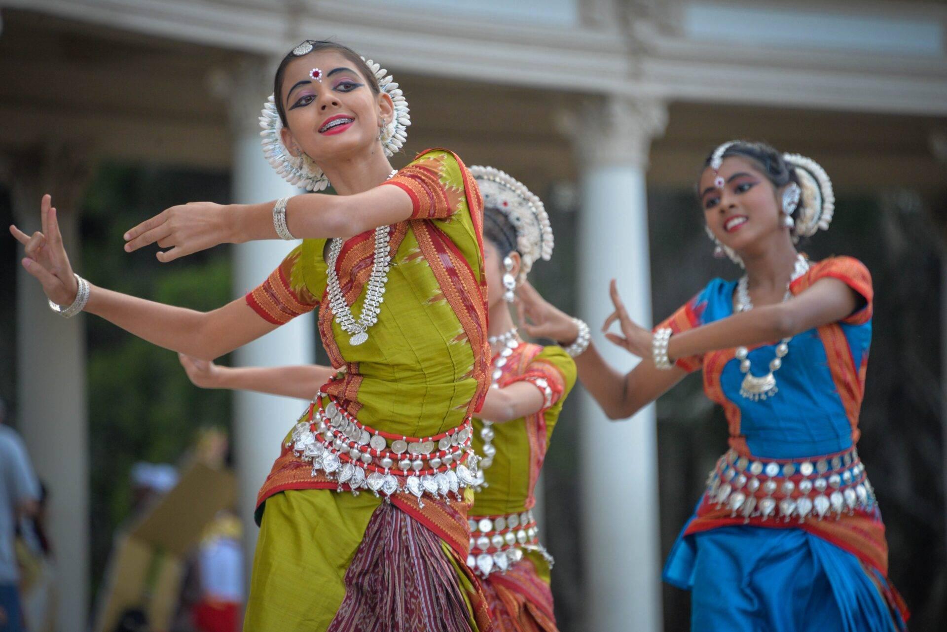 Danseuses en costumes traditionnels colorés exécutant une danse classique indienne devant une architecture coloniale