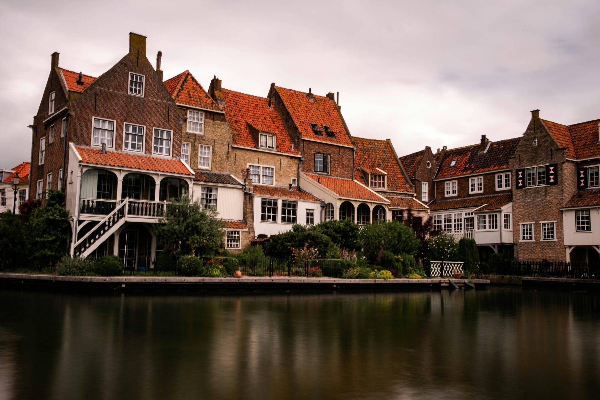 Rangée de maisons traditionnelles néerlandaises aux toits oranges bordant un canal calme sous un ciel nuageux