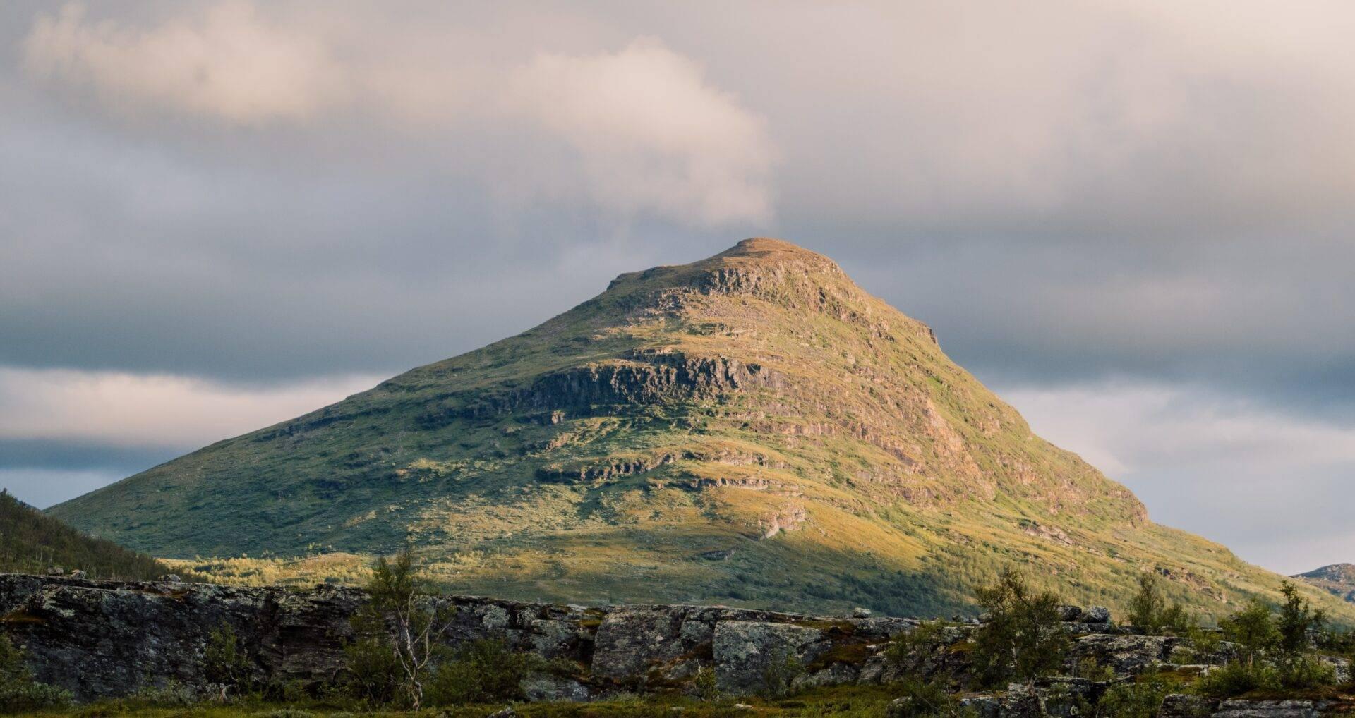 Une montagne conique aux pentes verdoyantes et rocheuses sous un ciel nuageux