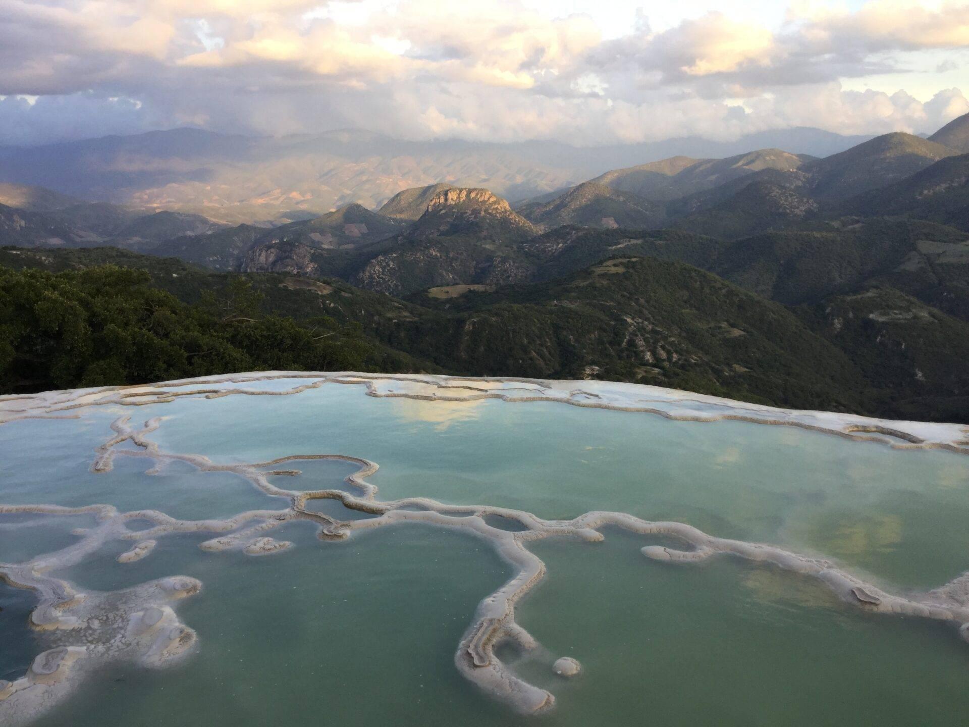 Terrasses thermales turquoise avec dépôts minéraux blancs dominant une vallée montagneuse verdoyante