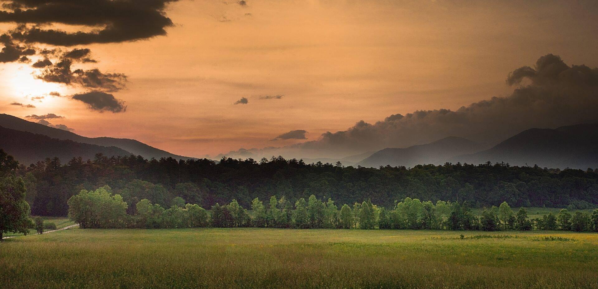 Vallée verdoyante au coucher de soleil avec montagnes boisées et ciel orangé dramatique
