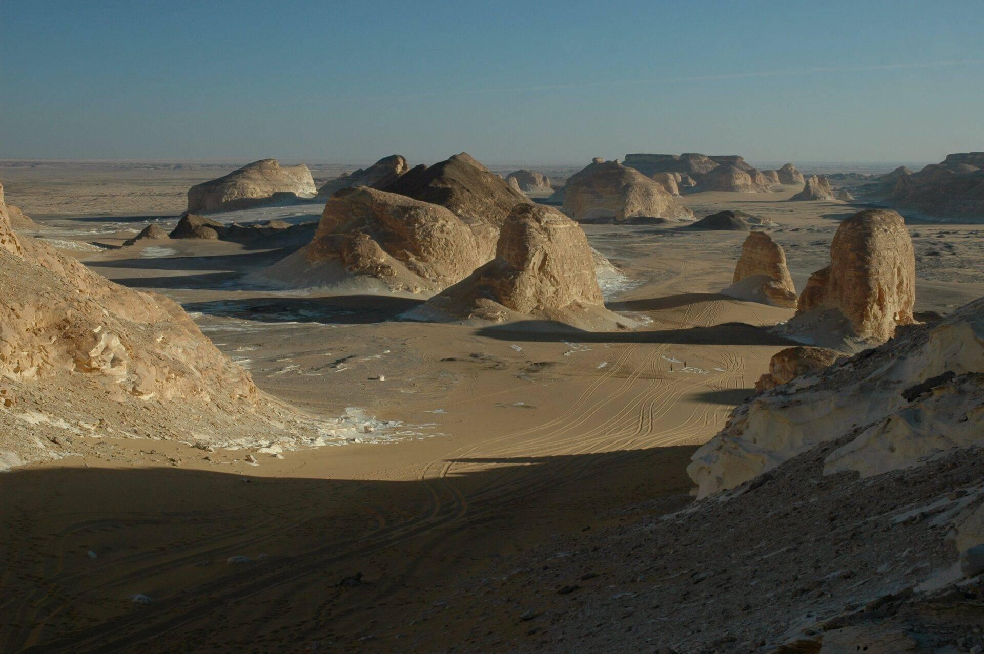 Formations rocheuses calcaires spectaculaires dans un désert aride avec traces de véhicules sur le sol sablonneux