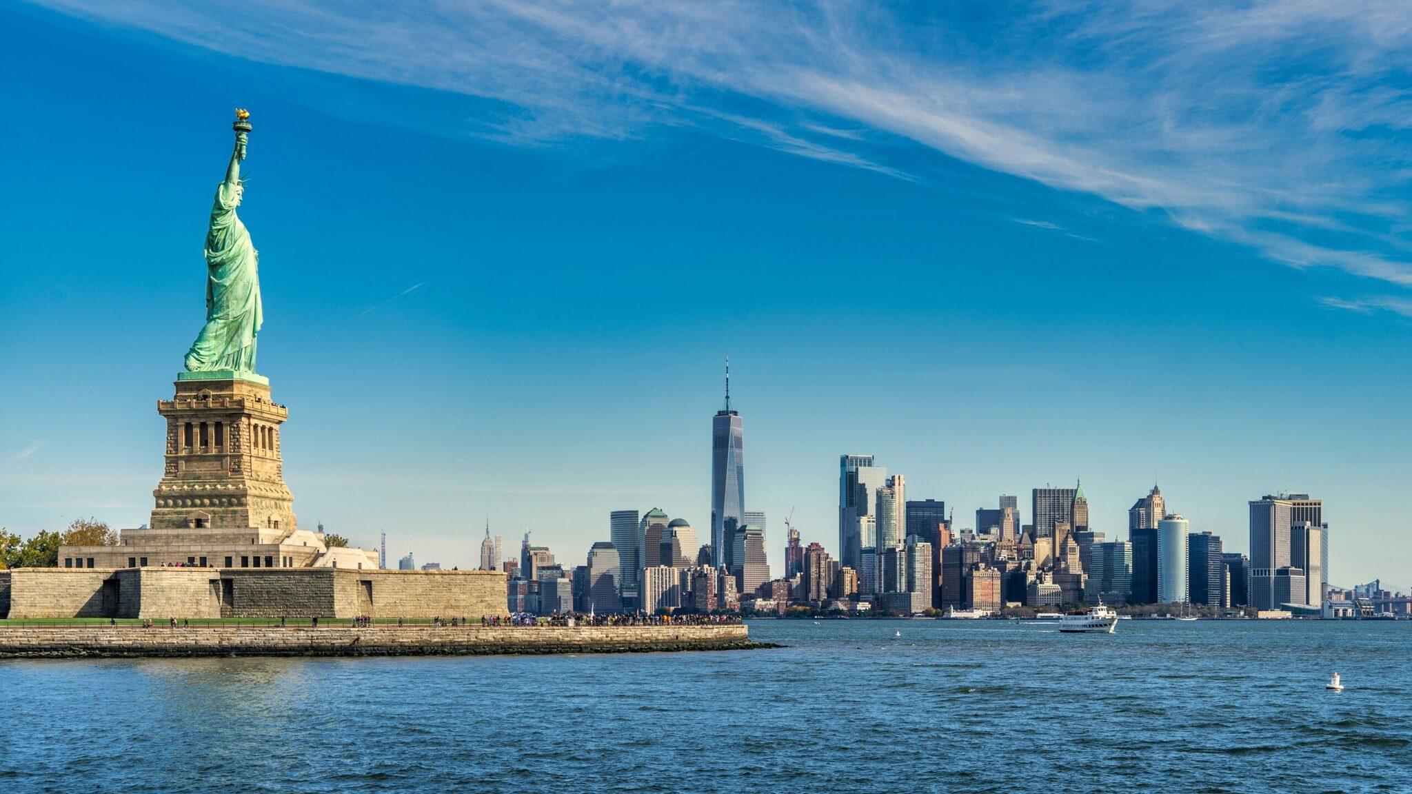 La Statue de la Liberté sur son île face aux gratte-ciel de Manhattan sous un ciel bleu dégagé