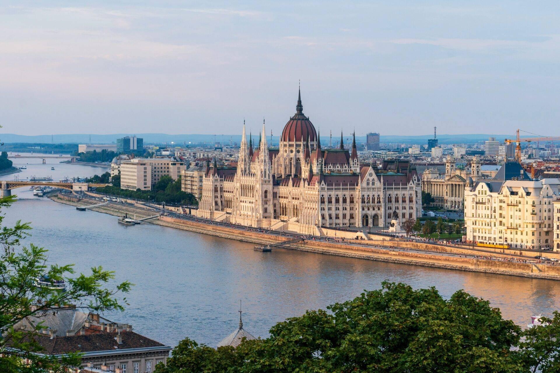 Vue panoramique d’un imposant bâtiment parlementaire aux dômes rouges surplombant un fleuve dans une ville européenne
